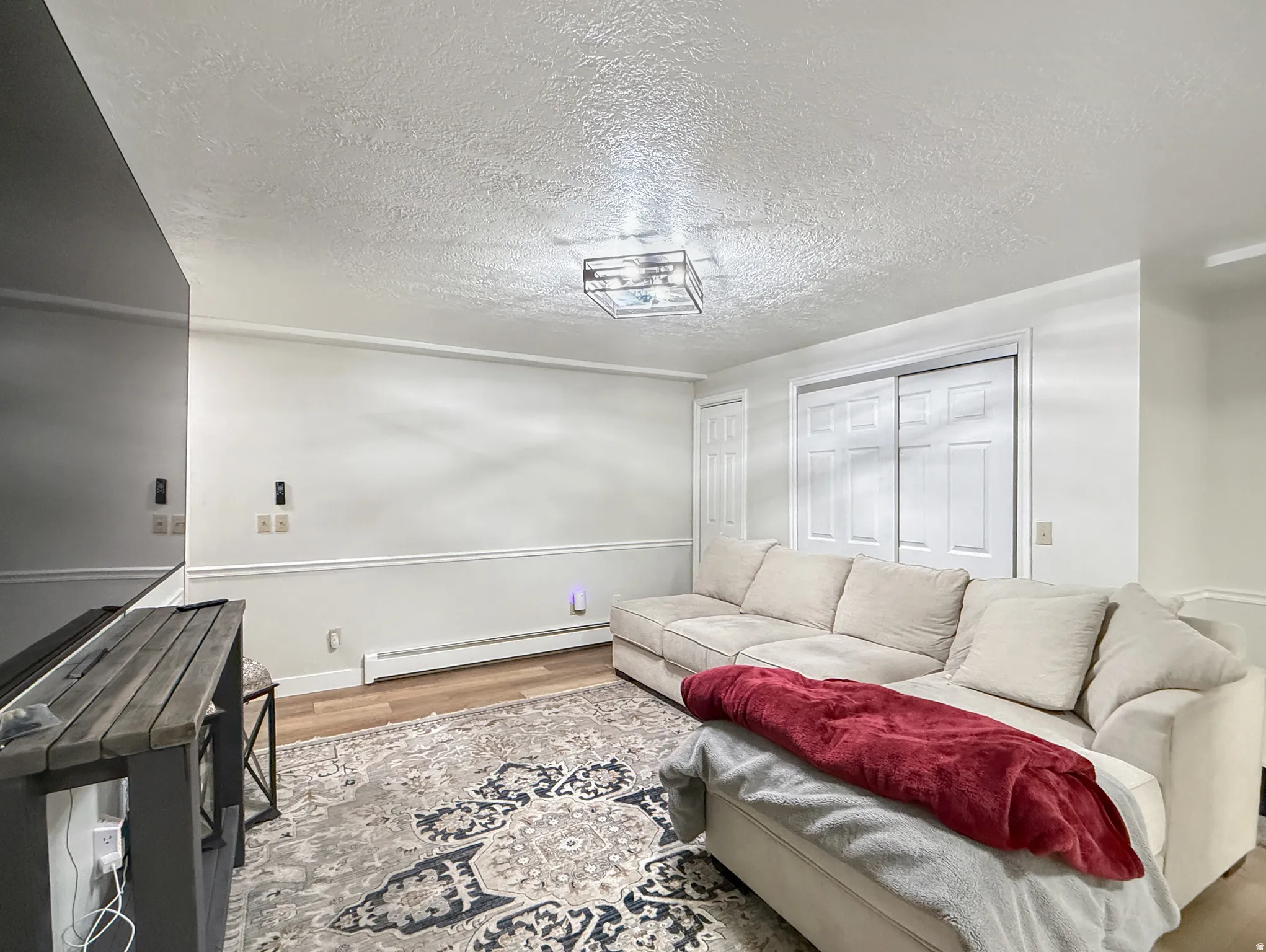 Living area with wood finished floors, a baseboard heating unit, and a textured ceiling
