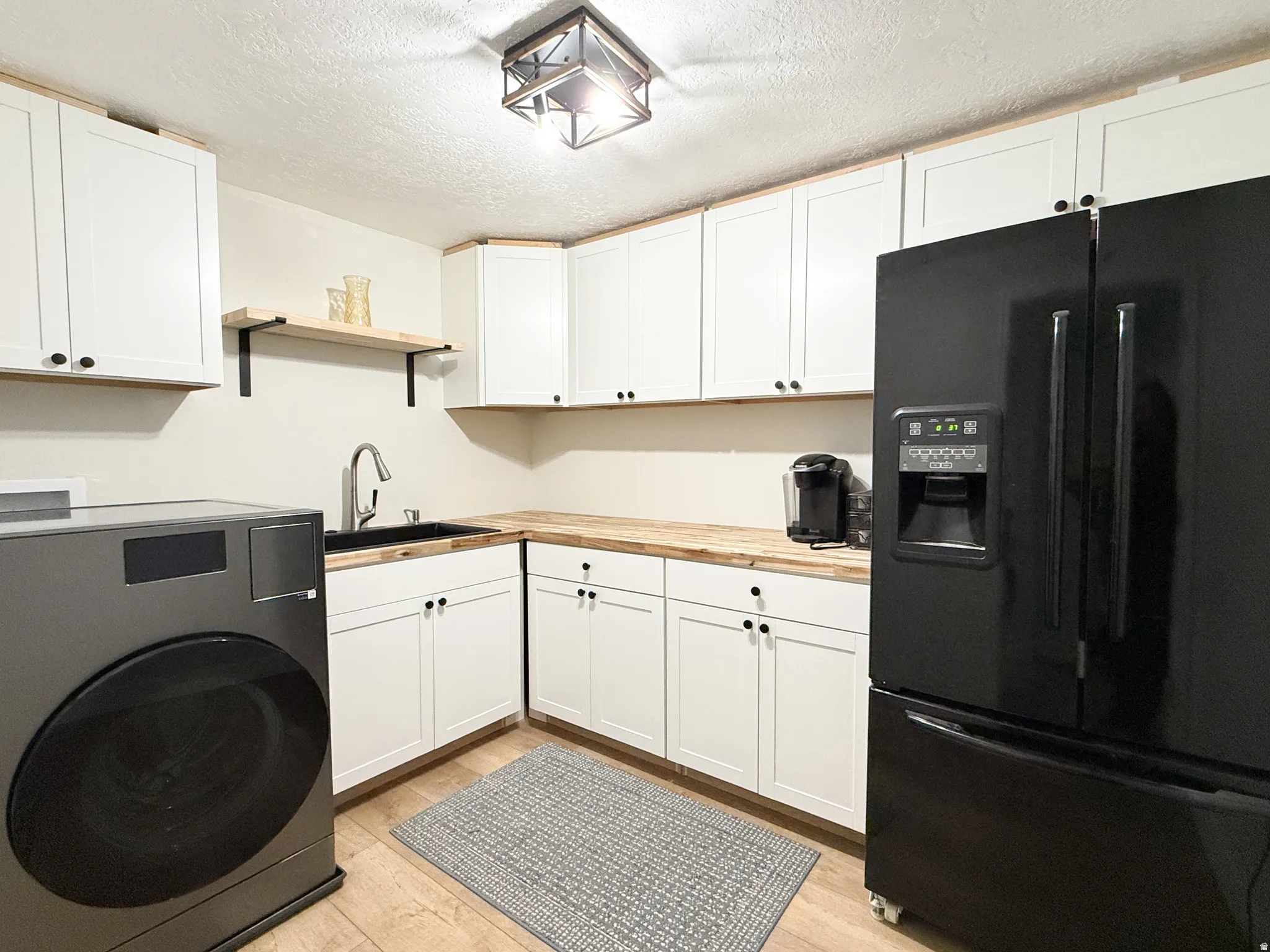Laundry area featuring washer / dryer, a textured ceiling, light wood finished floors, and cabinet space