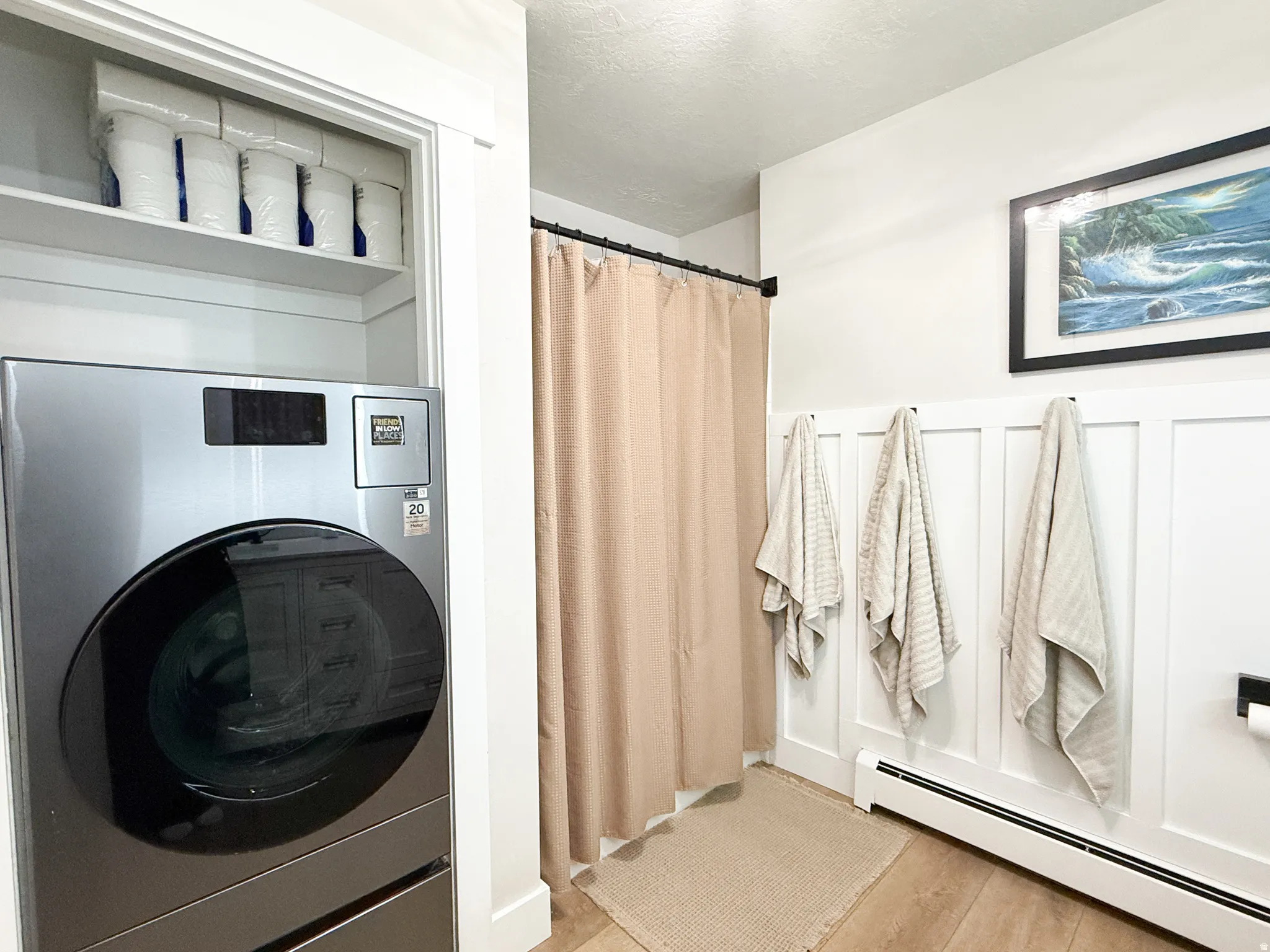 Laundry room featuring washer / clothes dryer, a baseboard radiator, light wood finished floors, a wainscoted wall, and a decorative wall