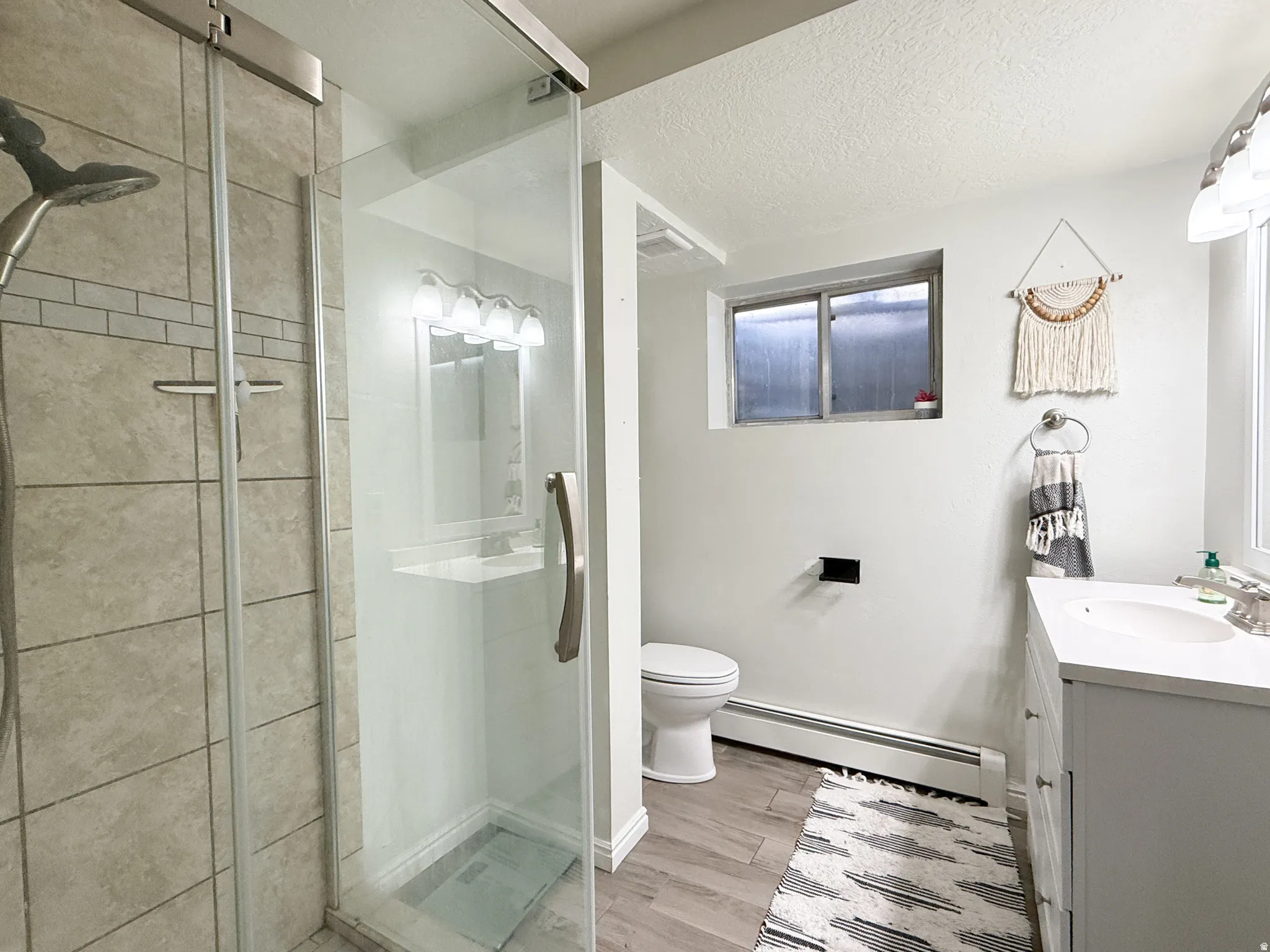 Bathroom with a shower stall, a baseboard heating unit, vanity, light wood-style floors, and a textured ceiling