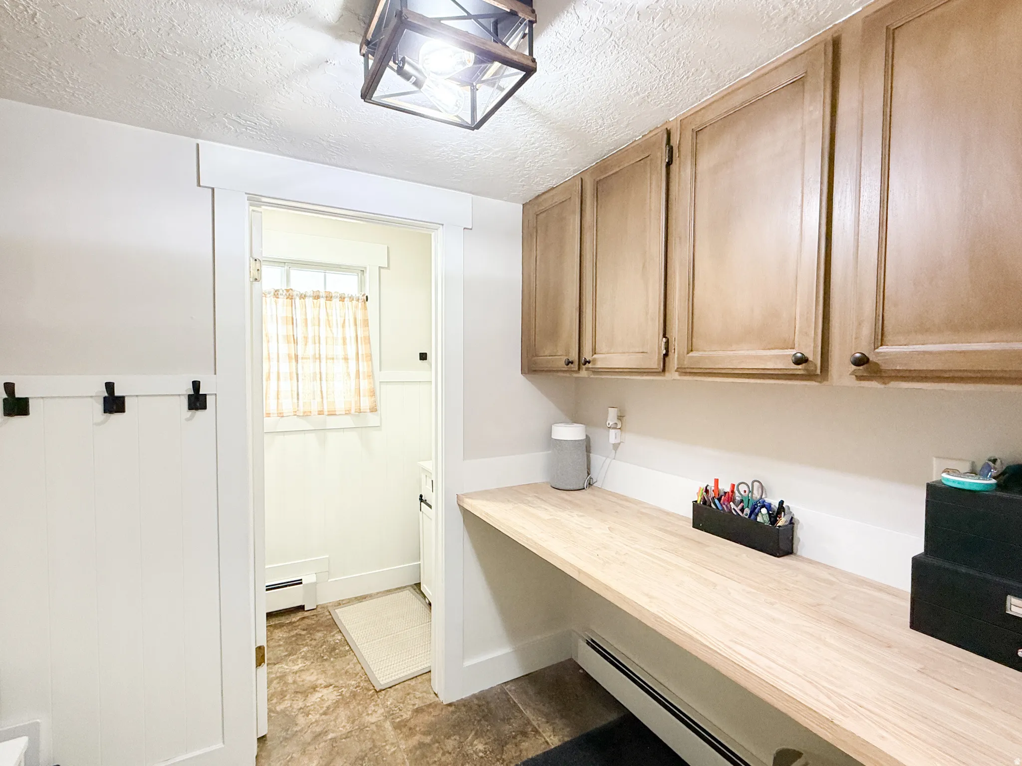 Office area with a textured ceiling, a baseboard heating unit, and wainscoting