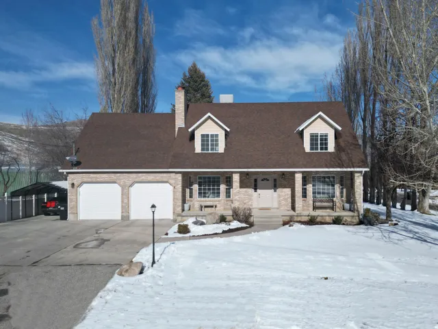 Cape cod-style house with covered porch, brick siding, an attached garage, concrete driveway, and a shingled roof