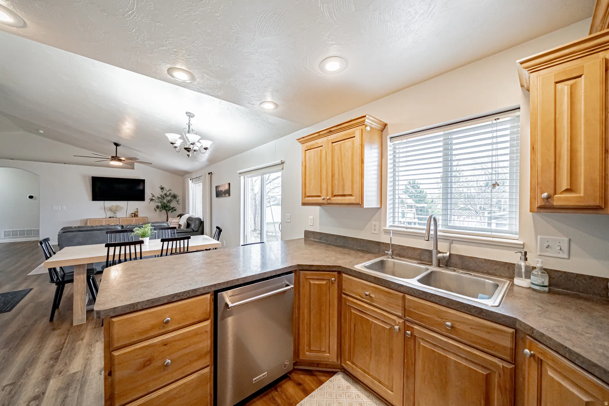 Kitchen featuring stainless steel dishwasher, a peninsula, open floor plan, light wood-type flooring, and lofted ceiling