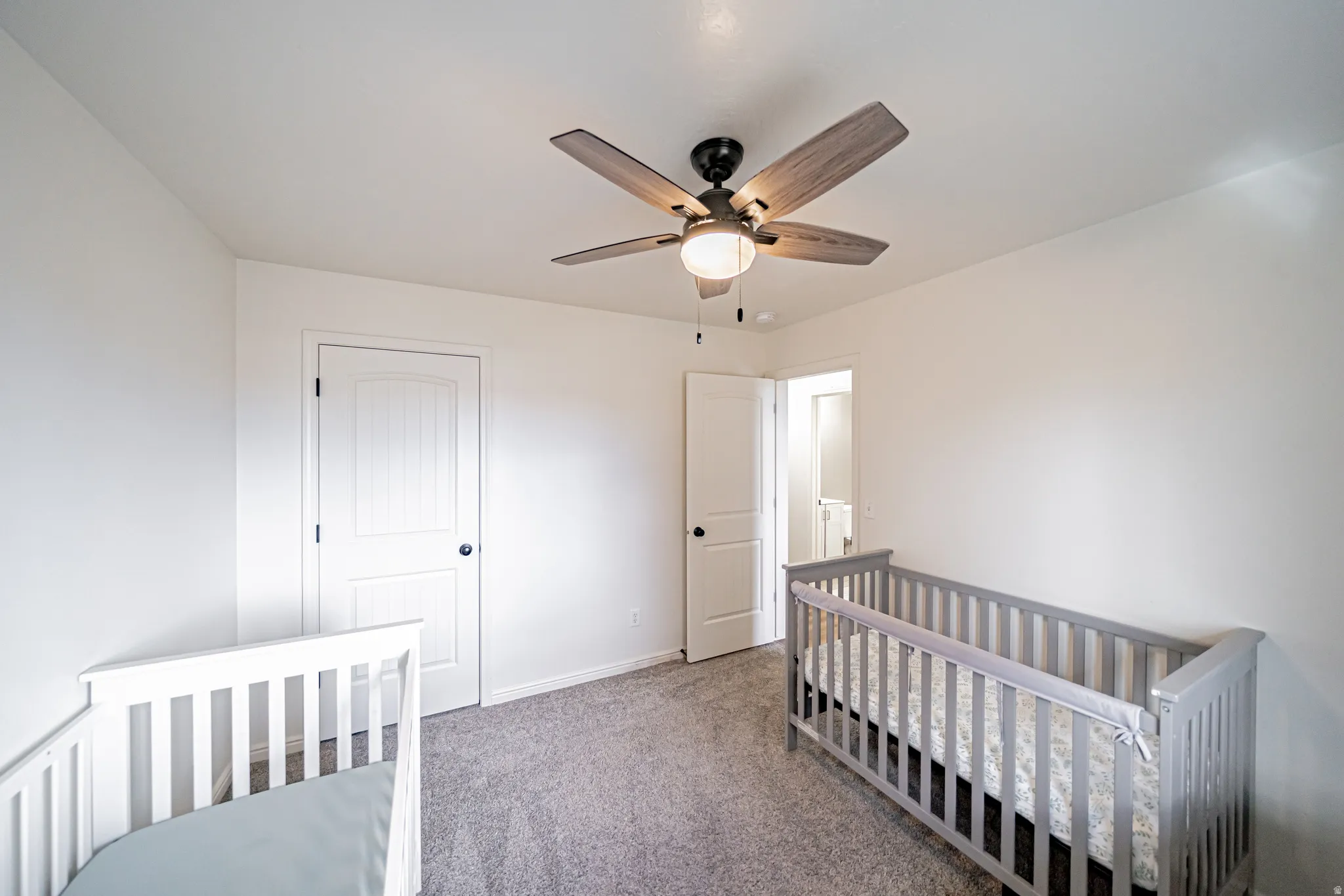 Bedroom with a nursery area, light carpet, and ceiling fan