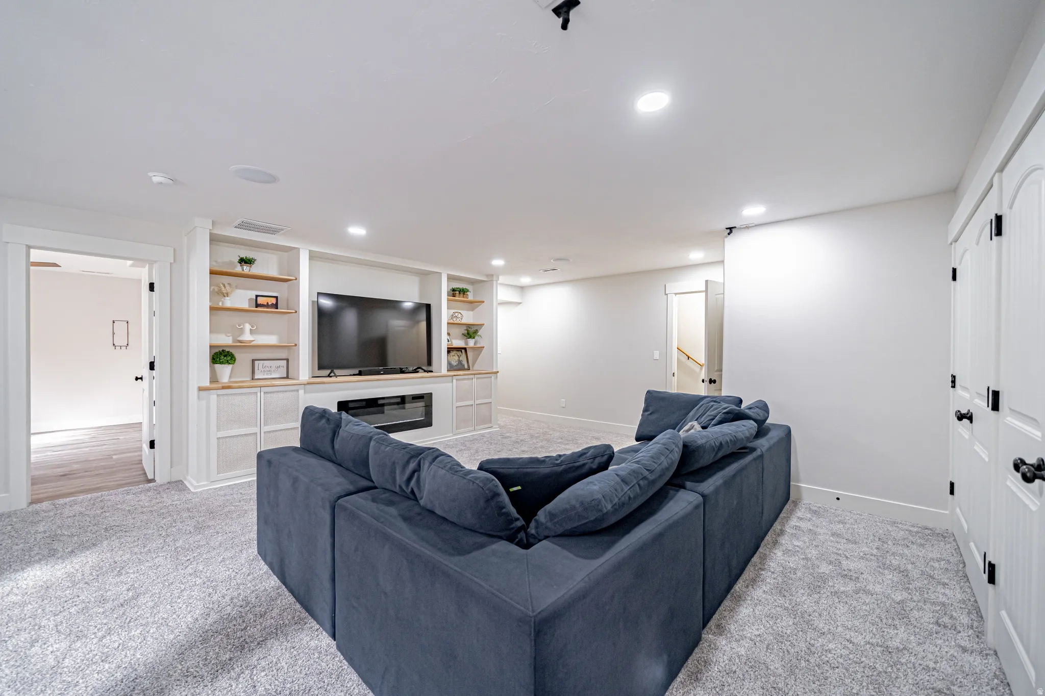 Living room with light colored carpet, a glass covered fireplace, recessed lighting, and built in features
