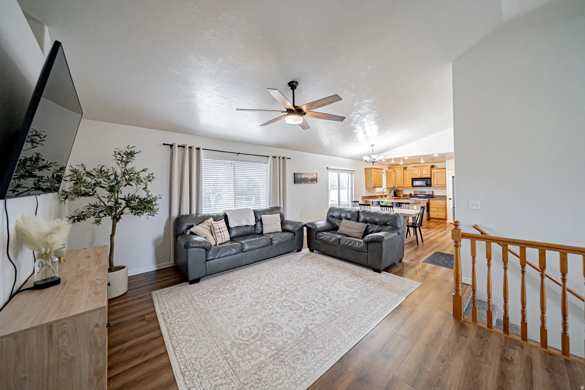 Living area featuring dark wood-style flooring, ceiling fan, vaulted ceiling, and hanging lights