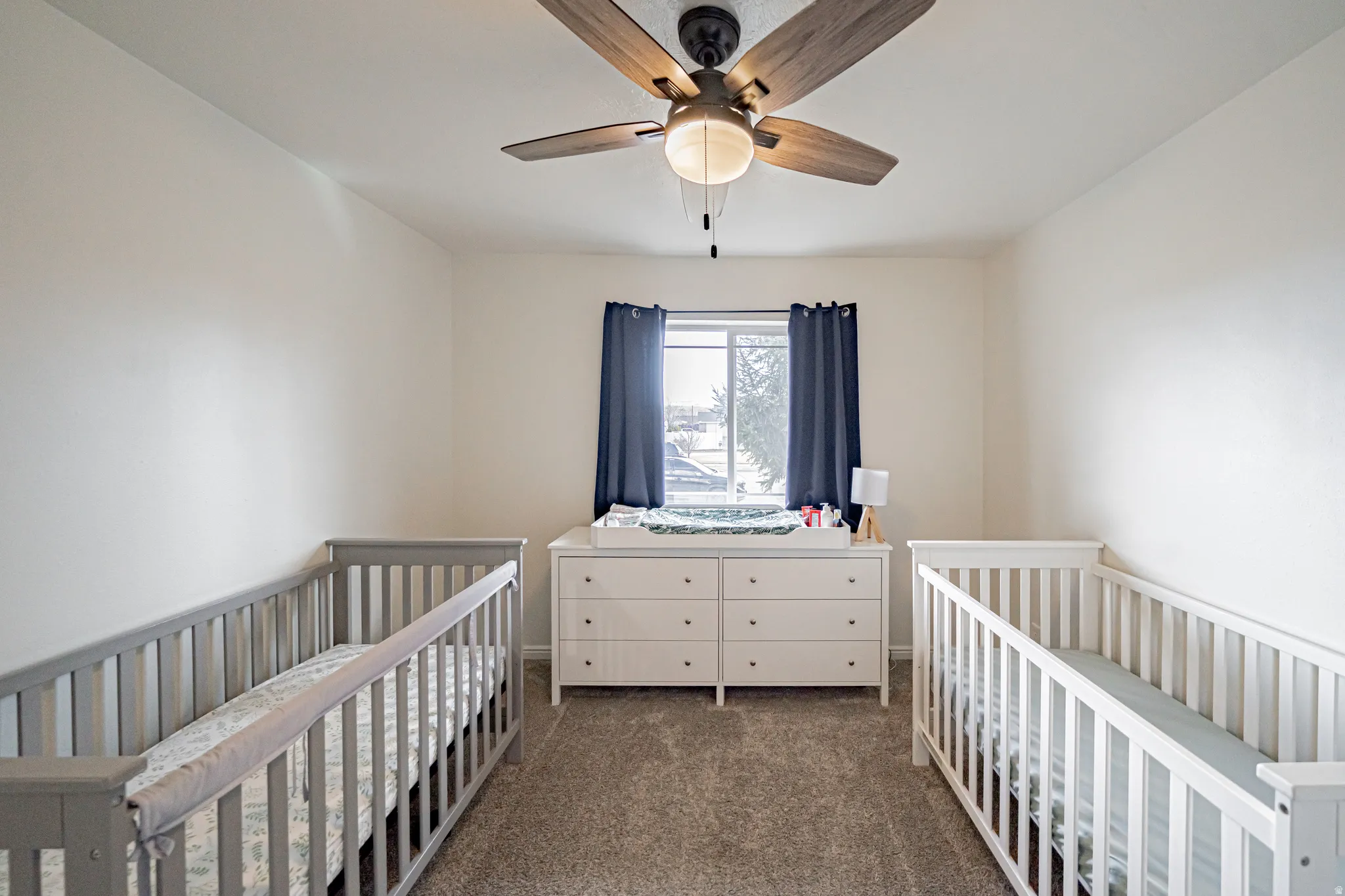 Bedroom featuring a crib, dark carpet, and ceiling fan