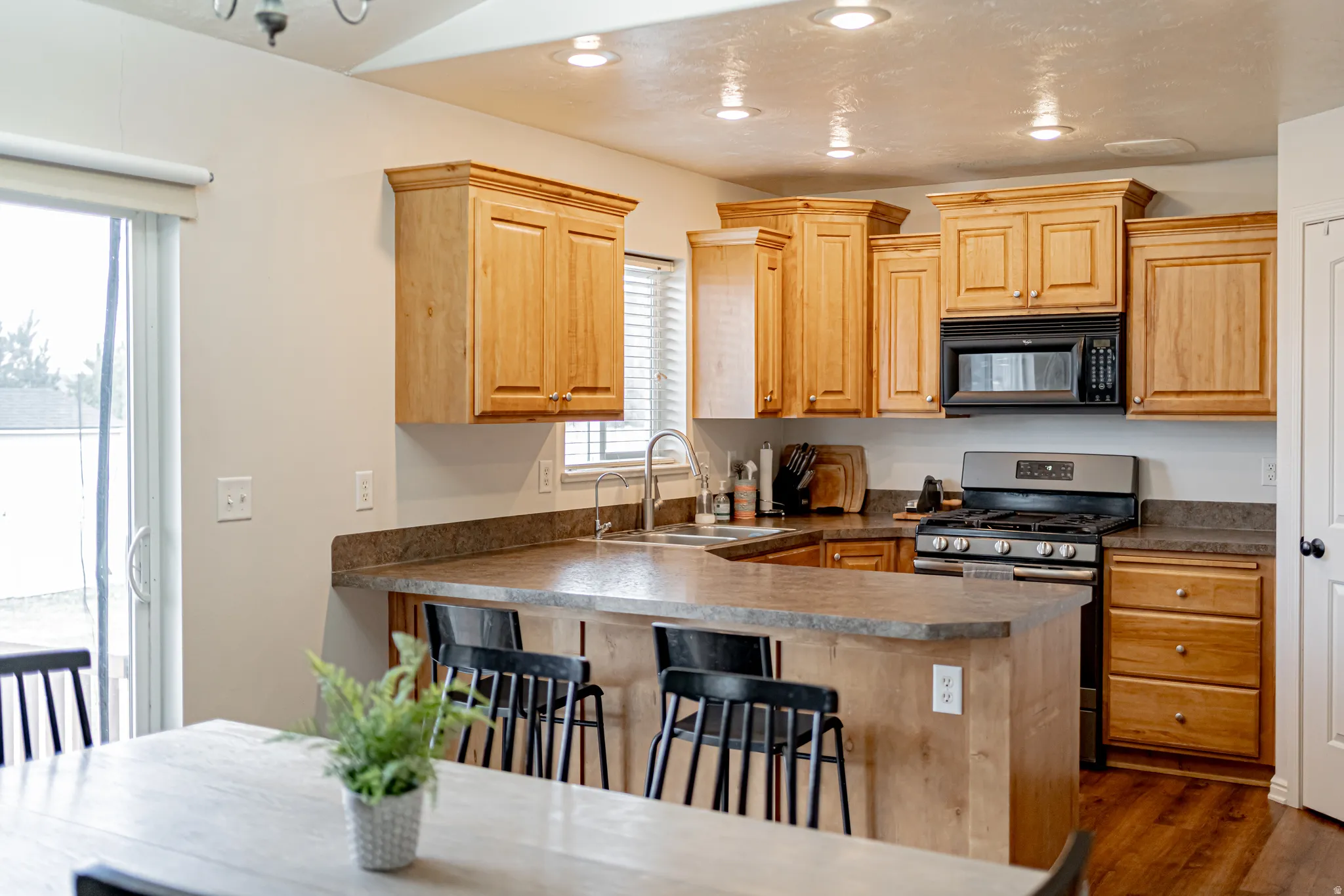 Kitchen featuring light wood finish cabinets, gas range, black microwave, a peninsula, and a breakfast bar area