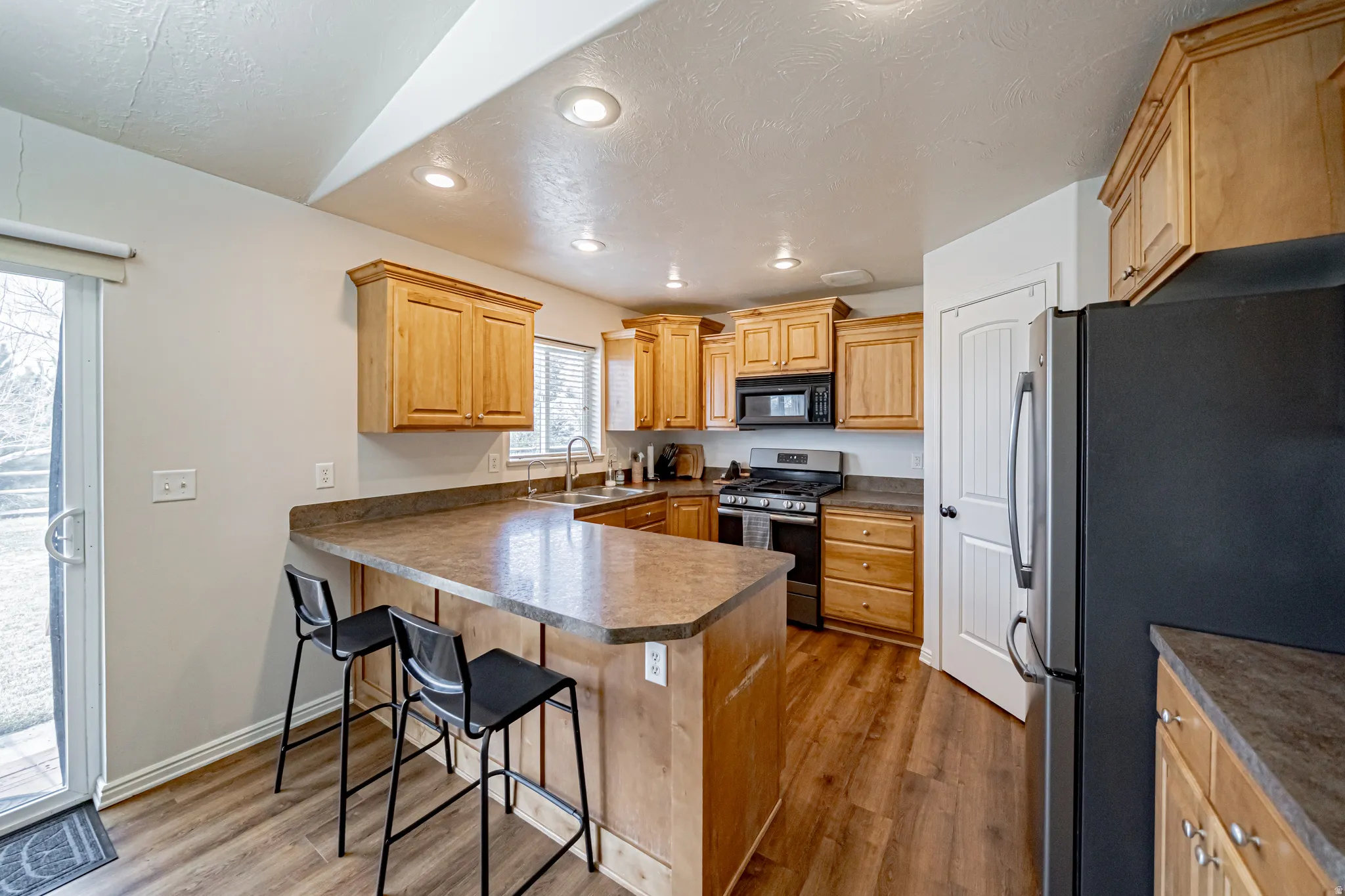 Kitchen with stainless steel appliances, a peninsula, a breakfast bar area, light wood finished floors, and recessed lighting
