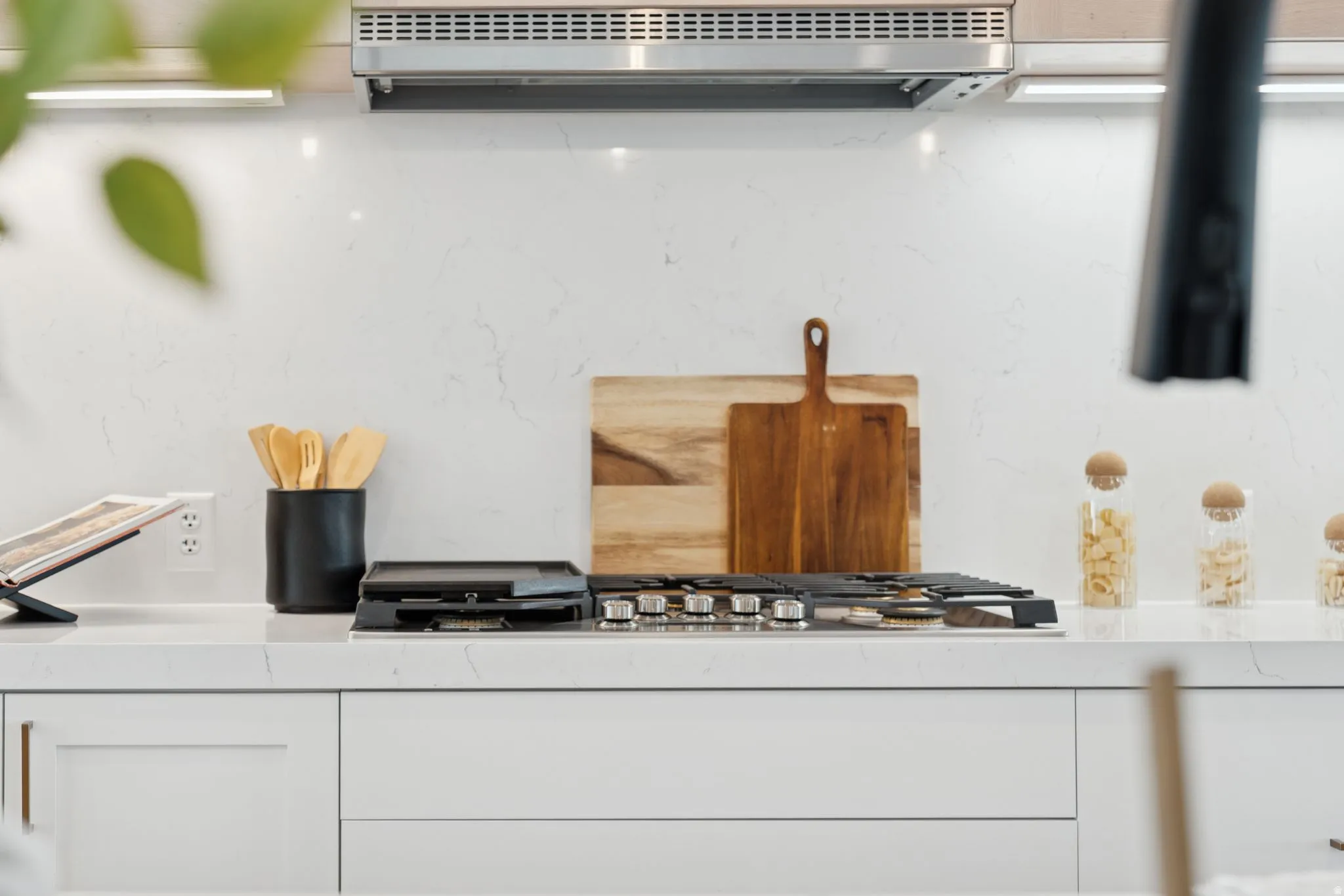 Kitchen view of white cabinets, stainless steel gas cooktop, and light stone countertops