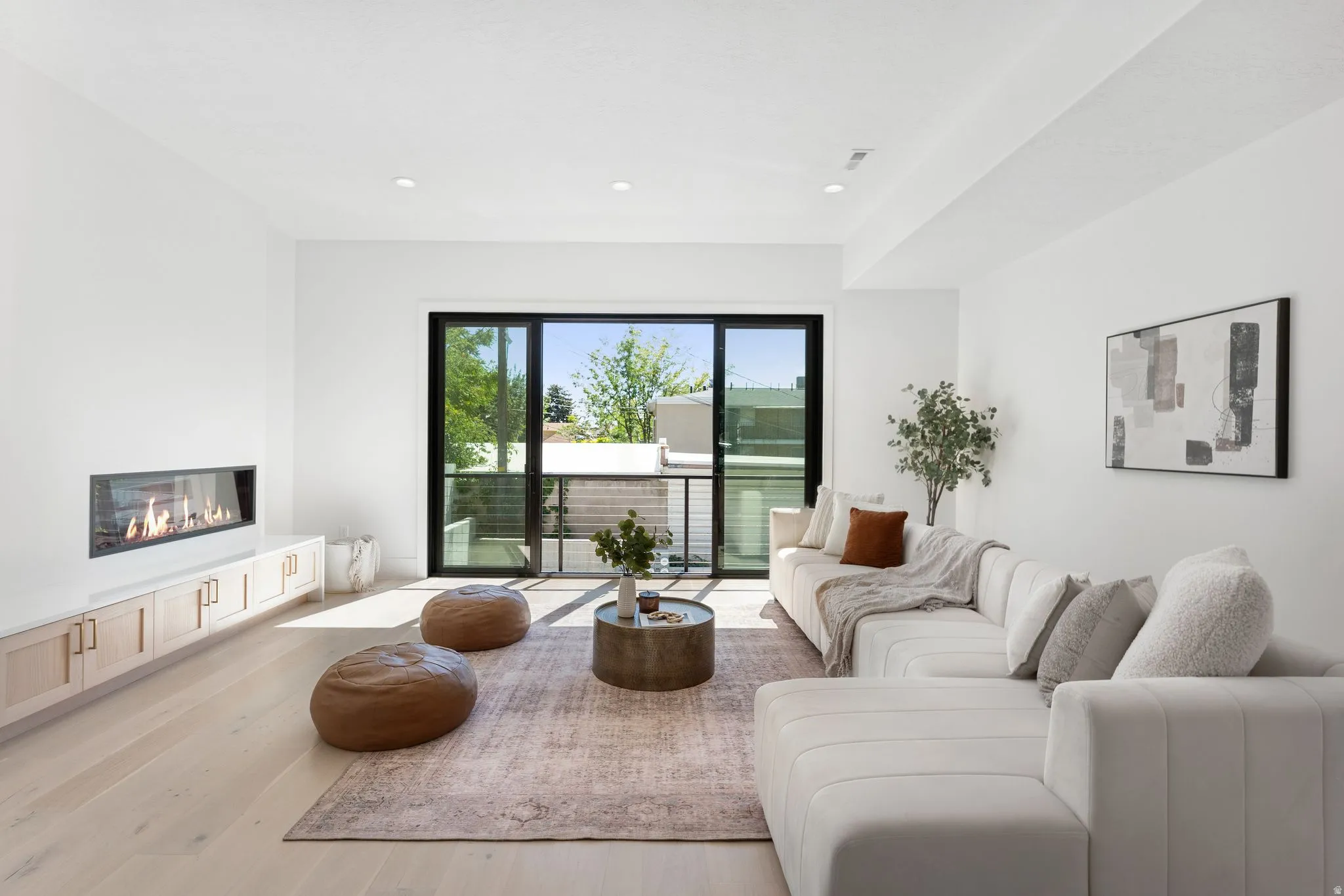 Living area with light wood-type flooring, a glass covered fireplace, and recessed lighting