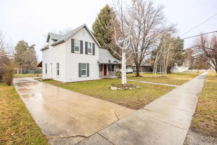 Traditional-style house with a front yard, covered porch, driveway, and roof with shingles