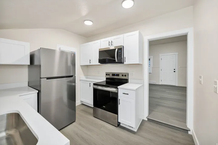 Kitchen featuring stainless steel appliances, white cabinetry, light wood-style floors, and lofted ceiling