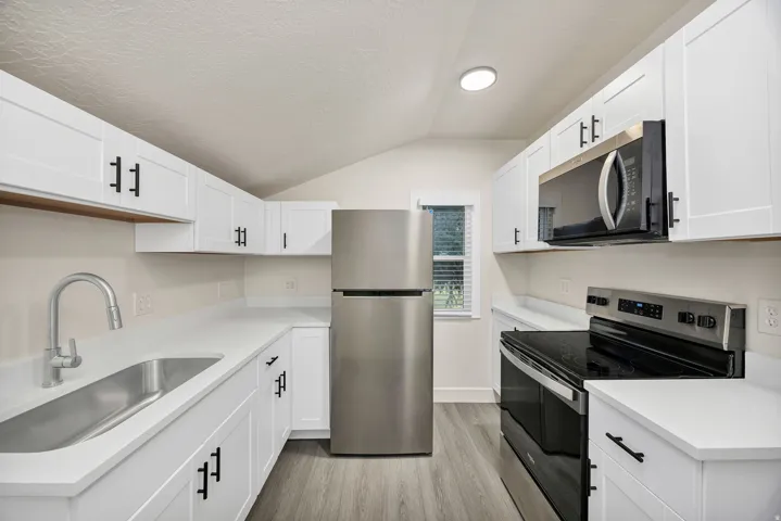 Kitchen featuring stainless steel appliances, white cabinets, light wood-style floors, and light stone countertops