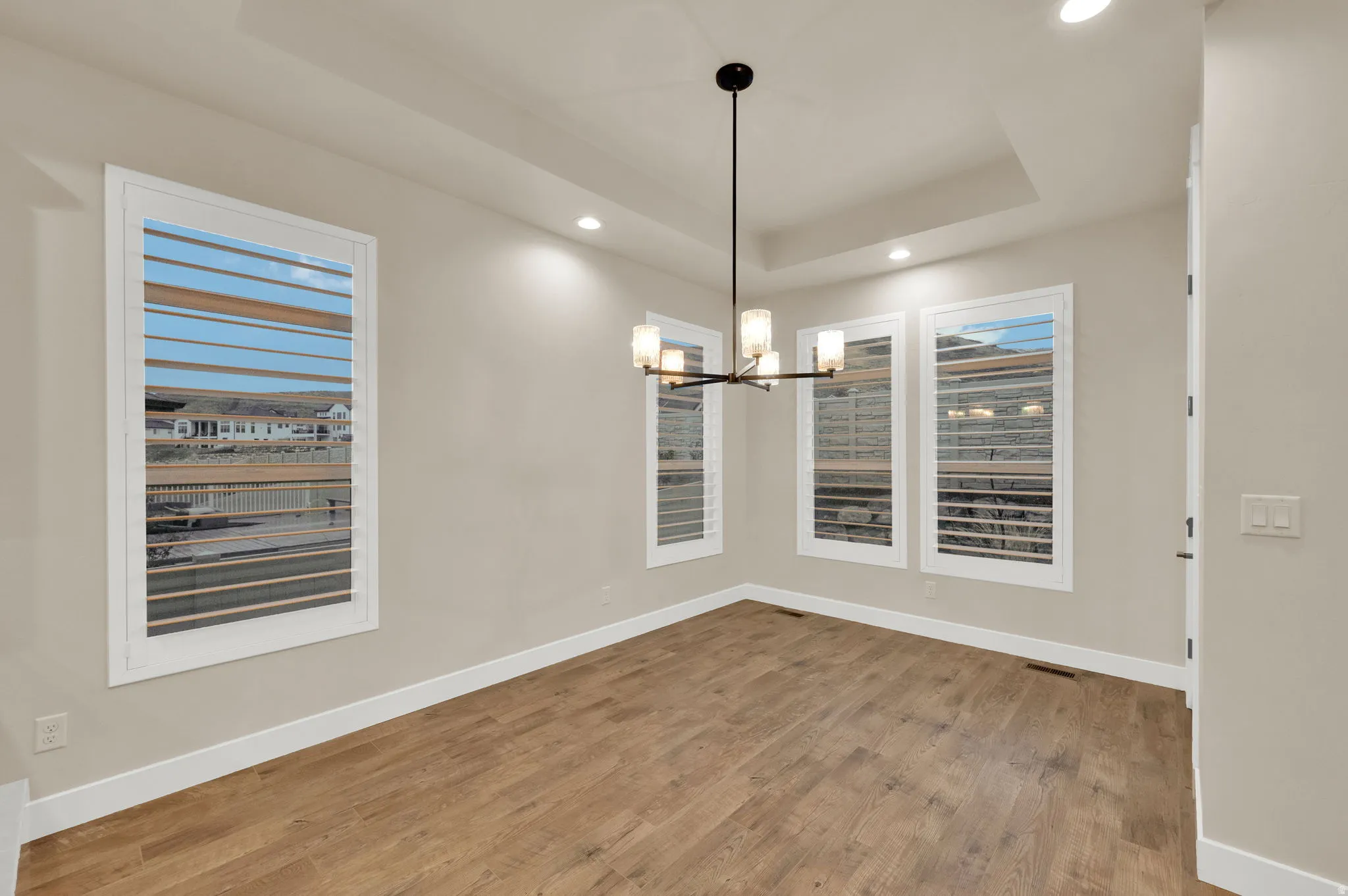 Unfurnished dining area featuring wood finished floors, a raised ceiling, and a chandelier