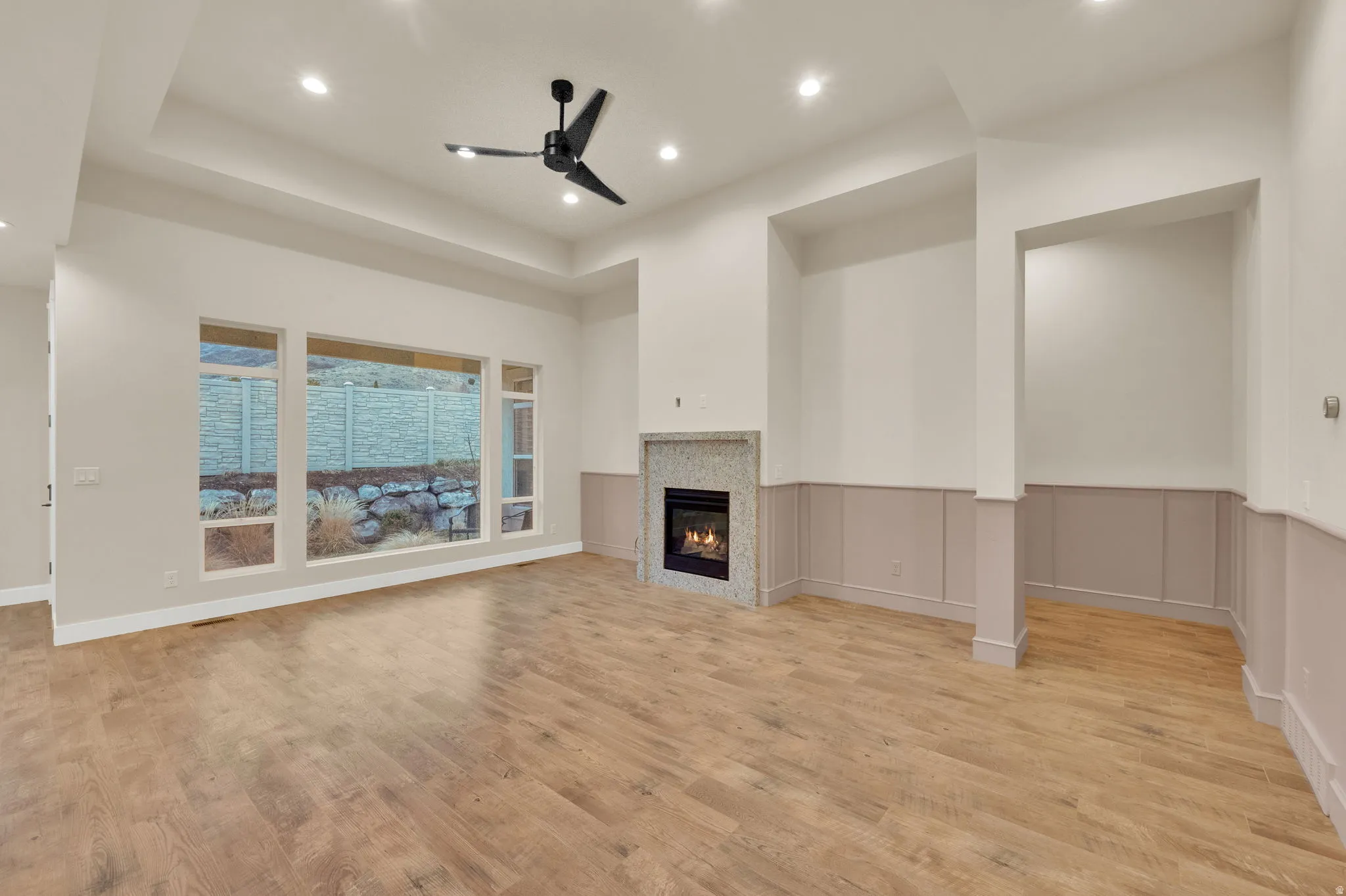 Unfurnished living room with a ceiling fan, a tile fireplace, light wood finished floors, recessed lighting, and a raised ceiling