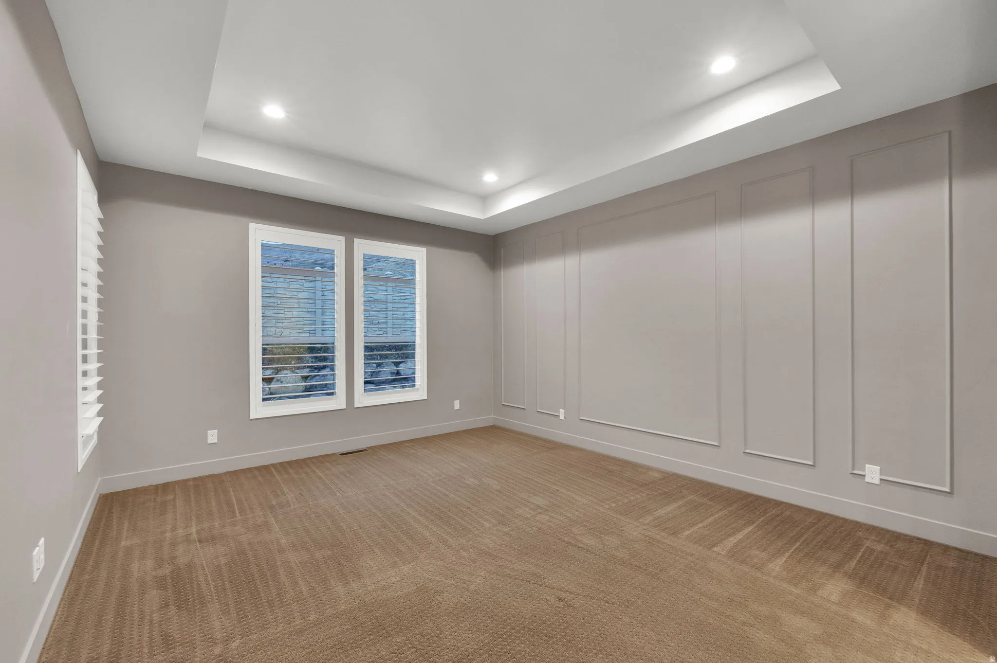 Empty room with recessed lighting, a raised ceiling, light colored carpet, and a decorative wall