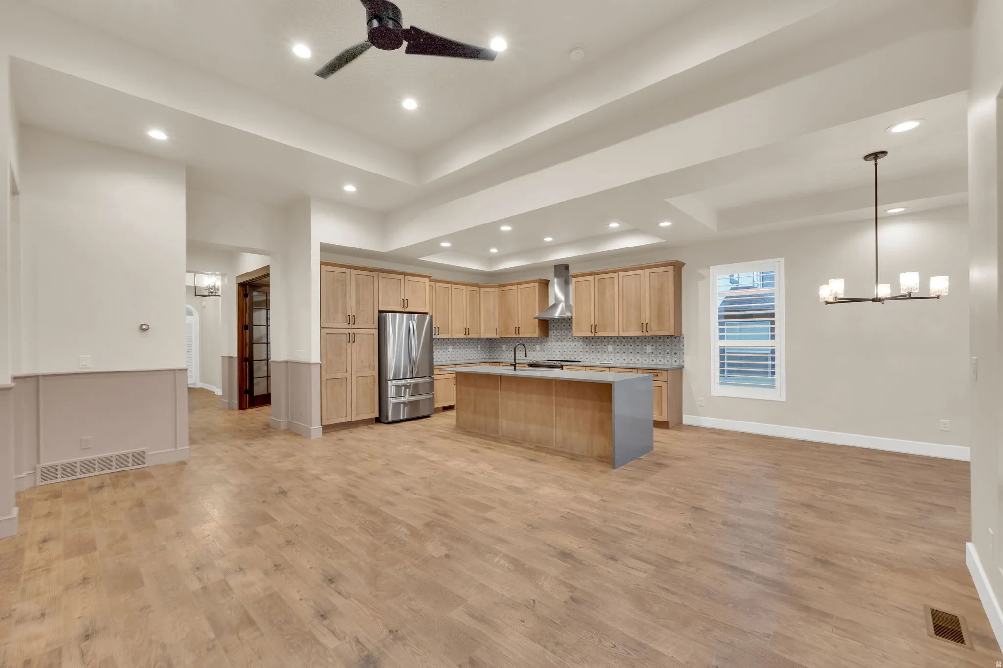 Kitchen featuring a tray ceiling, hanging lights, open floor plan, decorative backsplash, and a ceiling fan