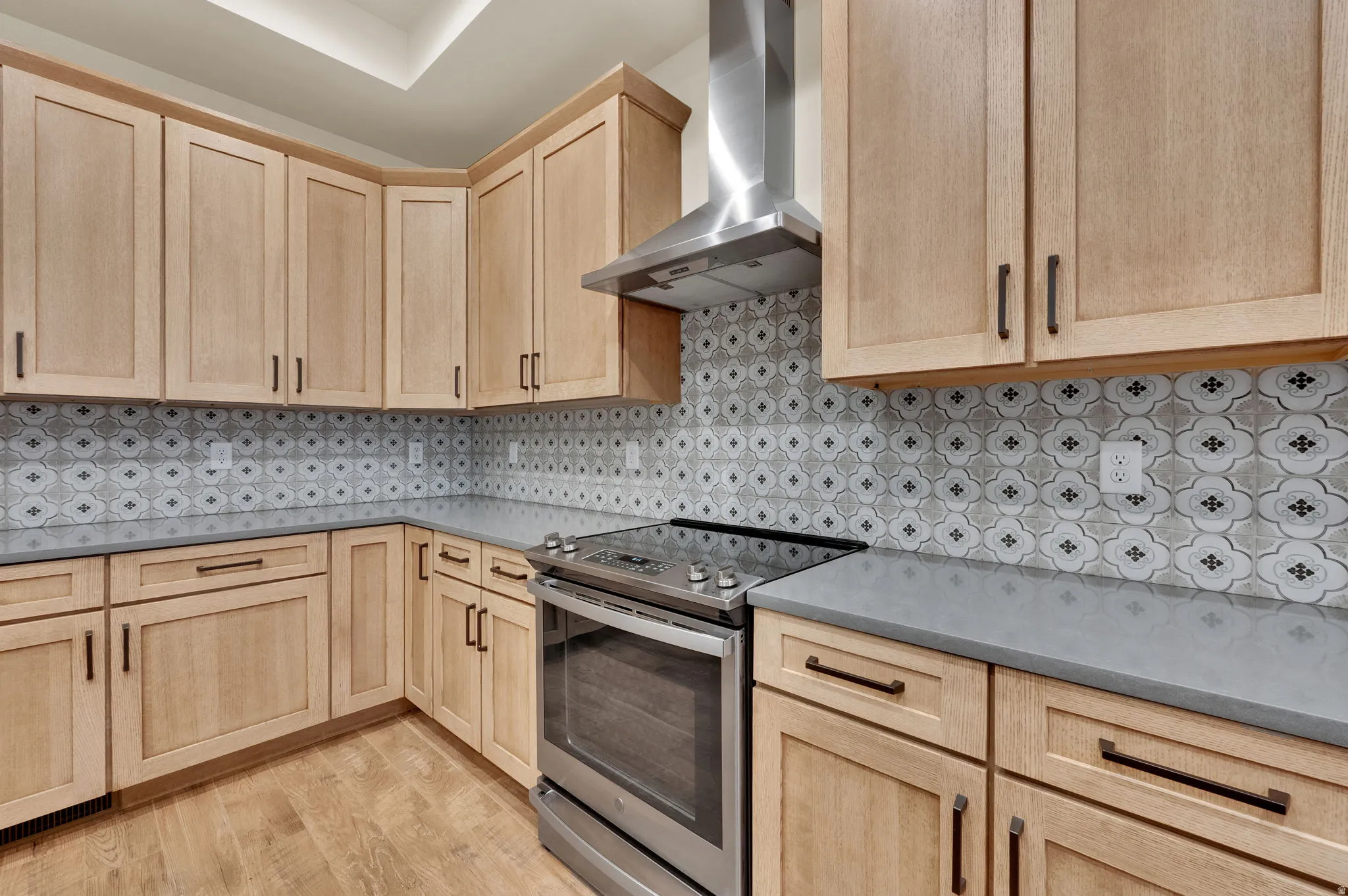 Kitchen with stainless steel electric stove, light wood finish cabinetry, light wood finished floors, and decorative backsplash