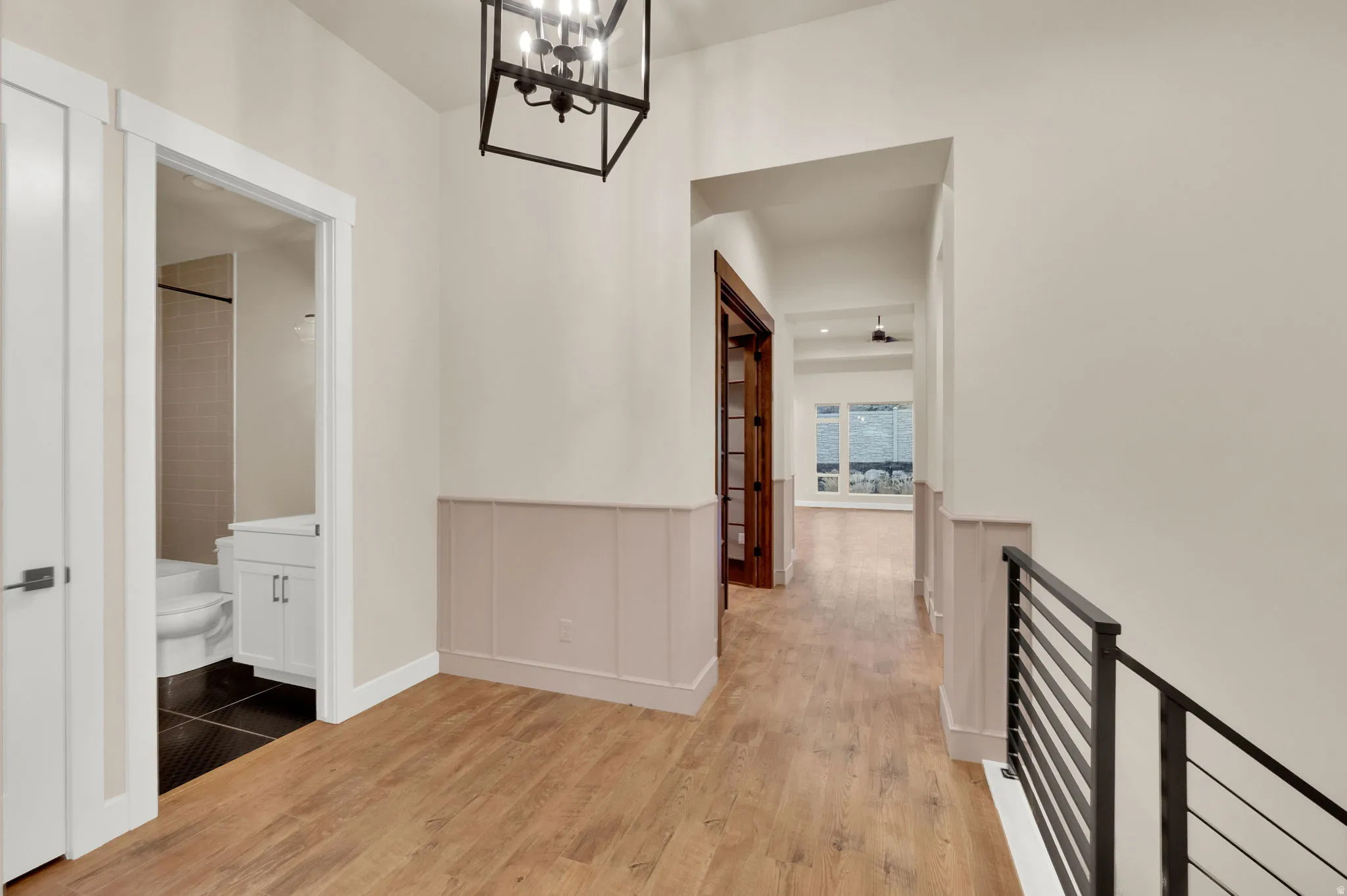 Hall with light wood finished floors, hanging lights, and wainscoting