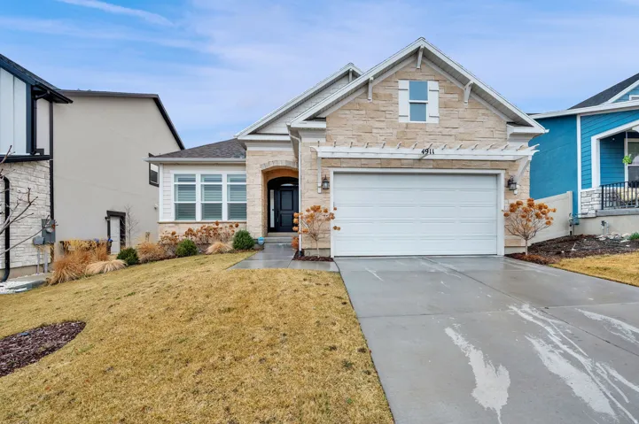 View of front of property with concrete driveway, stone siding, a garage, and a front lawn