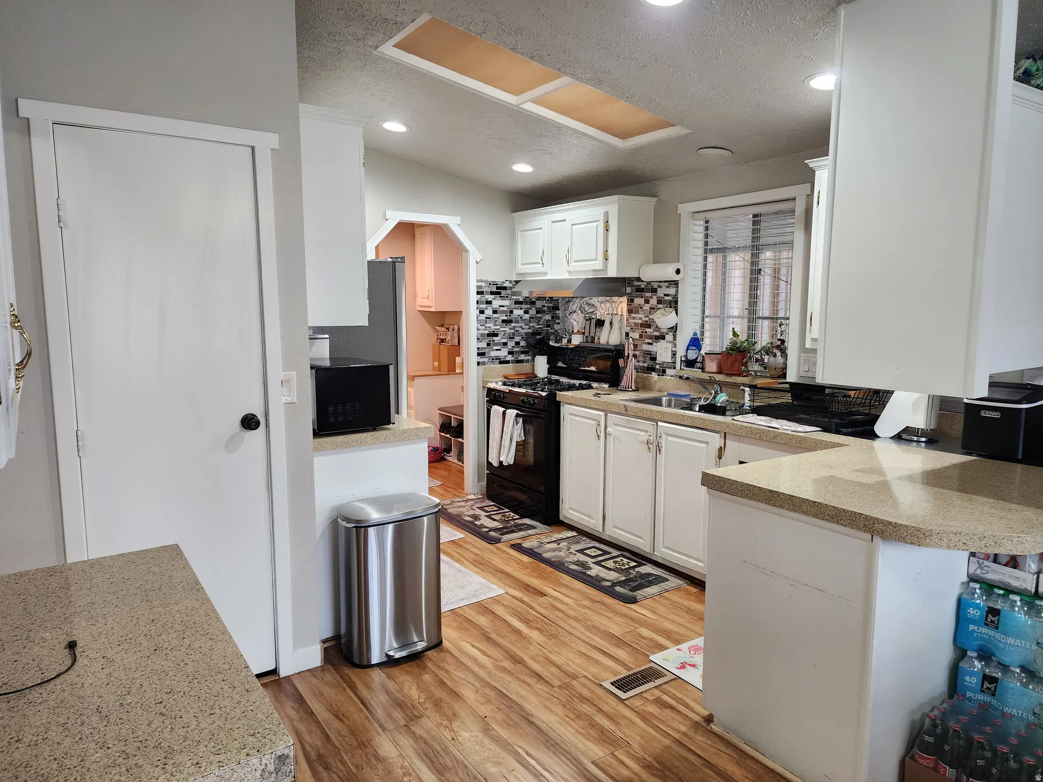 Kitchen with white cabinetry, black gas stove, a textured ceiling, light wood-type flooring, and decorative backsplash