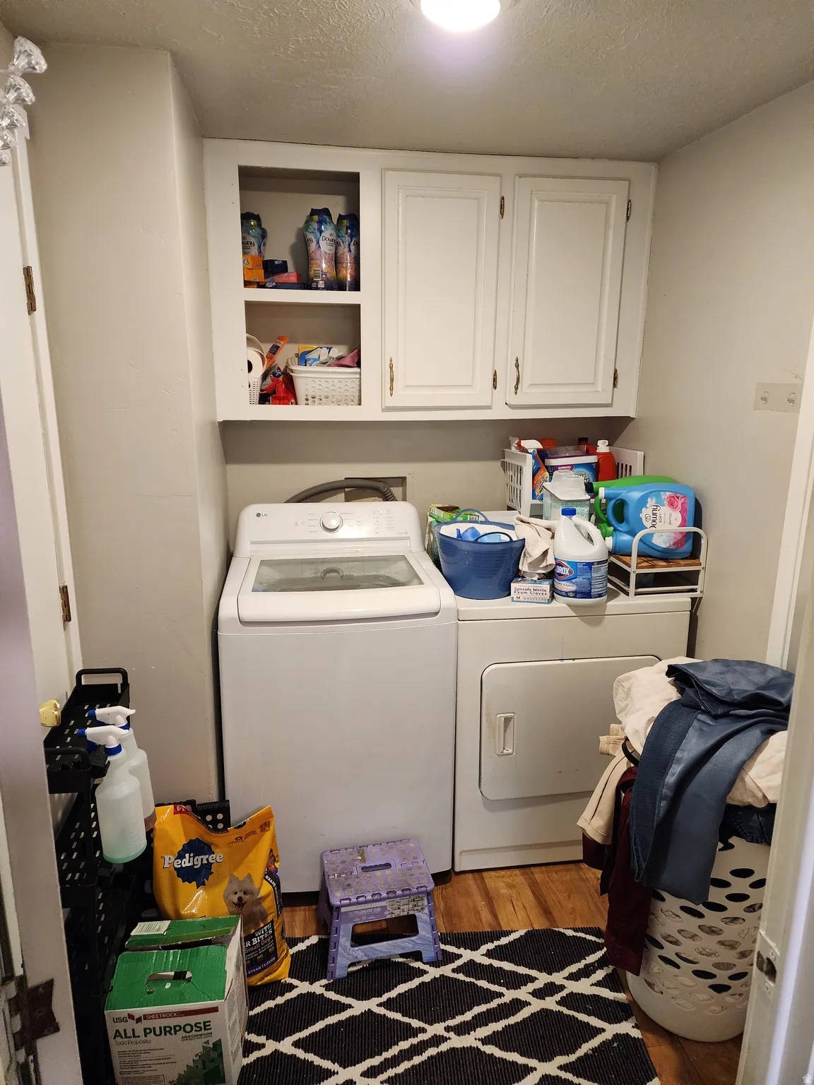 Laundry room featuring light wood finished floors, a textured ceiling, washing machine and dryer, and cabinet space