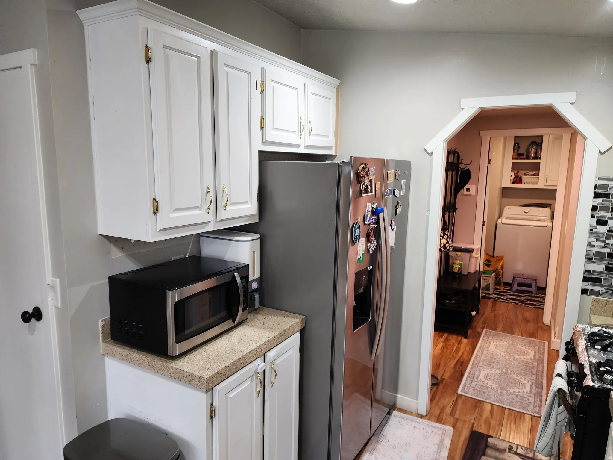 Kitchen featuring white cabinets, stainless steel appliances, washer / dryer, light countertops, and light wood-style floors