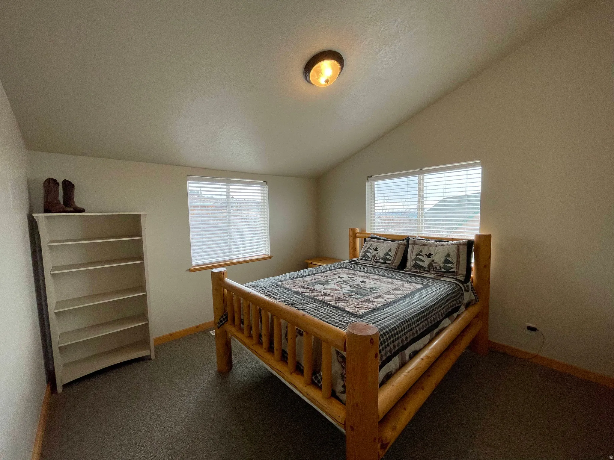 Bedroom with lofted ceiling, multiple windows, and dark colored carpet