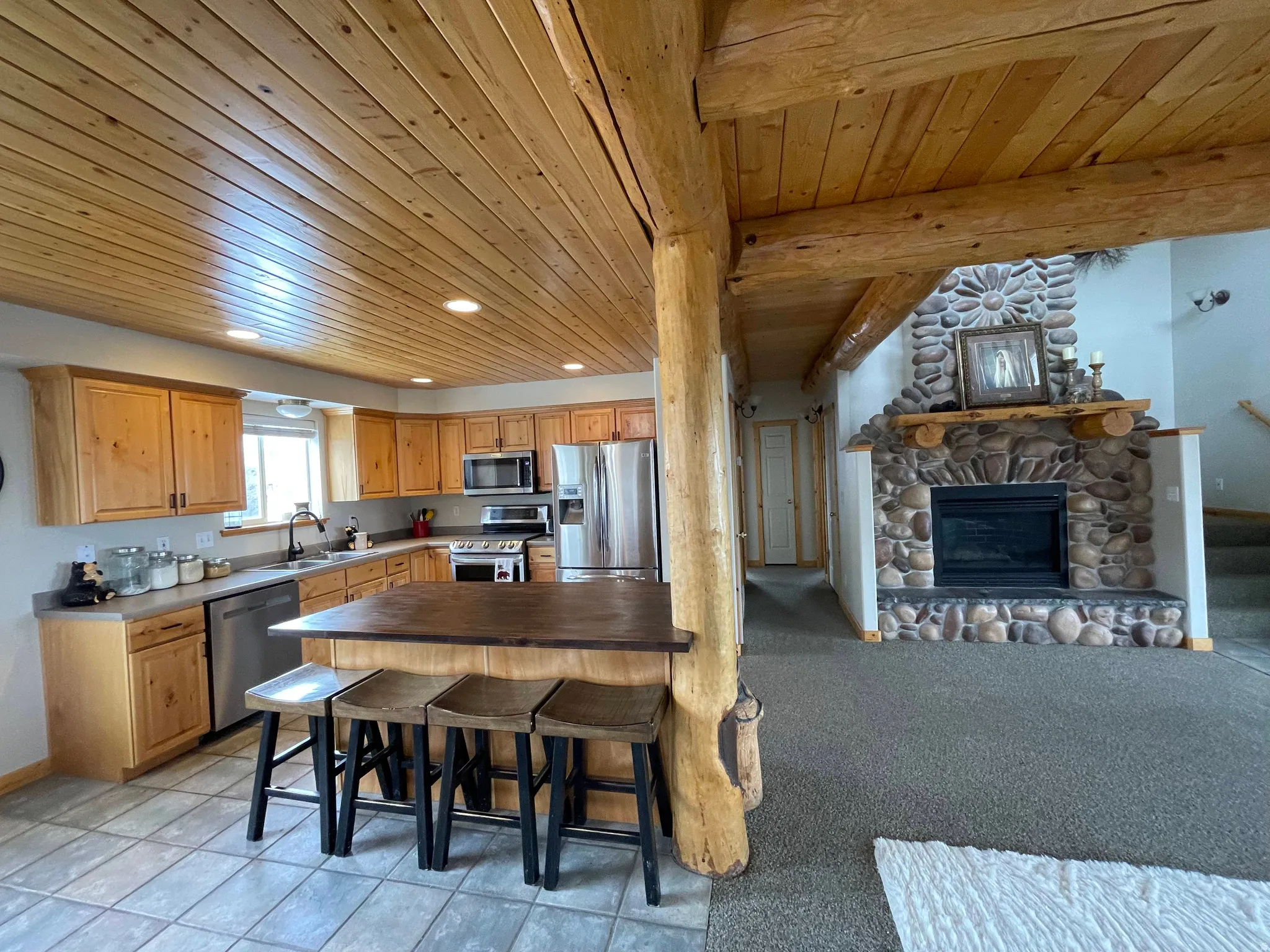 Kitchen featuring stainless steel appliances, recessed lighting, a stone fireplace, open floor plan, and wood ceiling