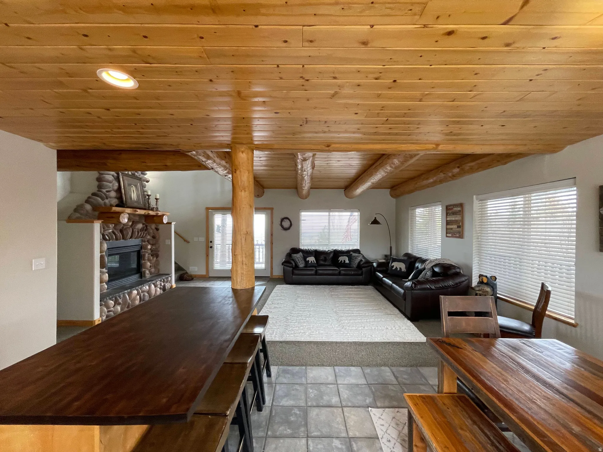 Living room featuring a wood ceiling with exposed beams, a stone fireplace, and recessed lighting