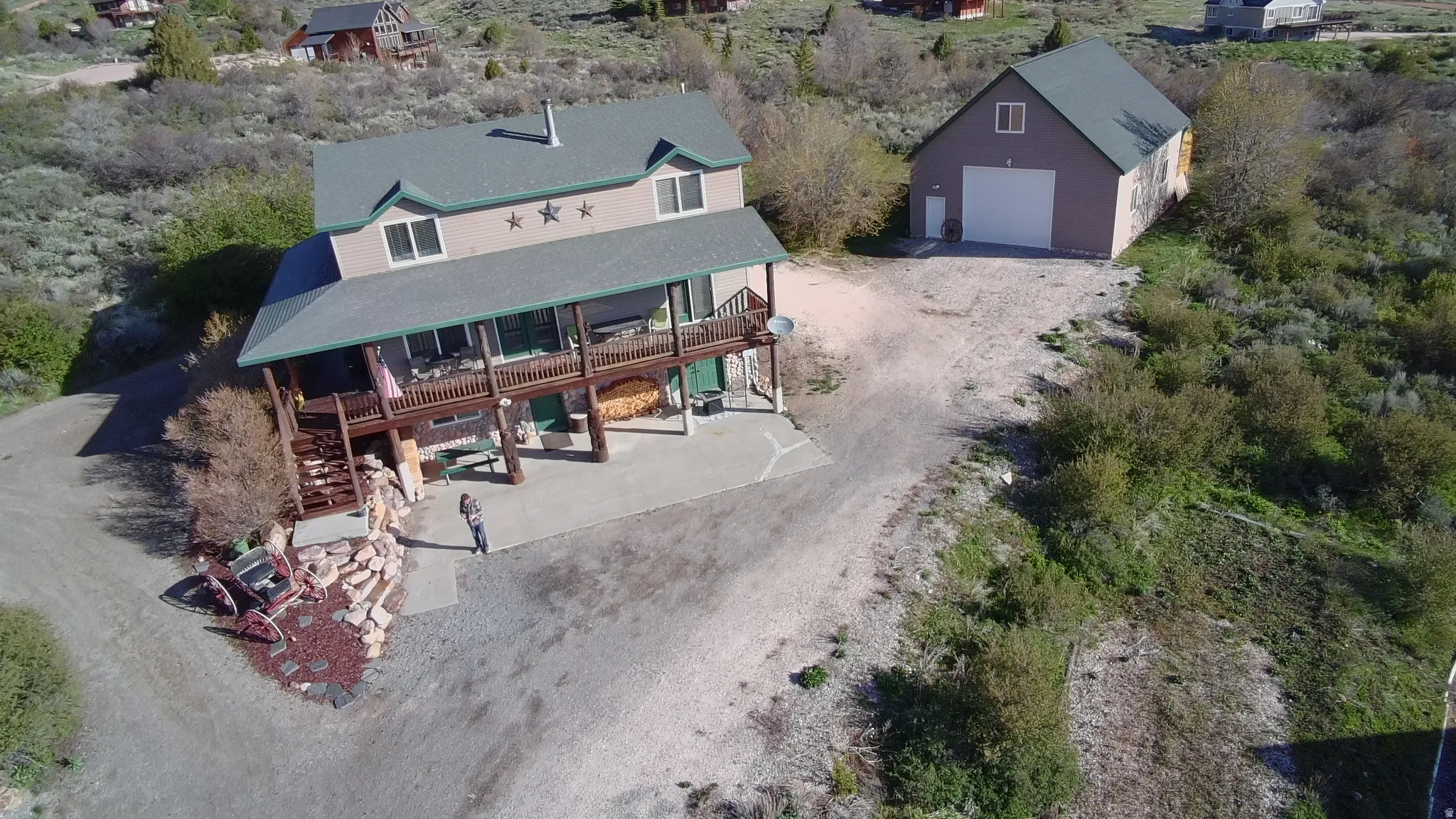 Two-story residential structure with a prominent upper-level balcony, adjacent detached garage, and a gravel driveway