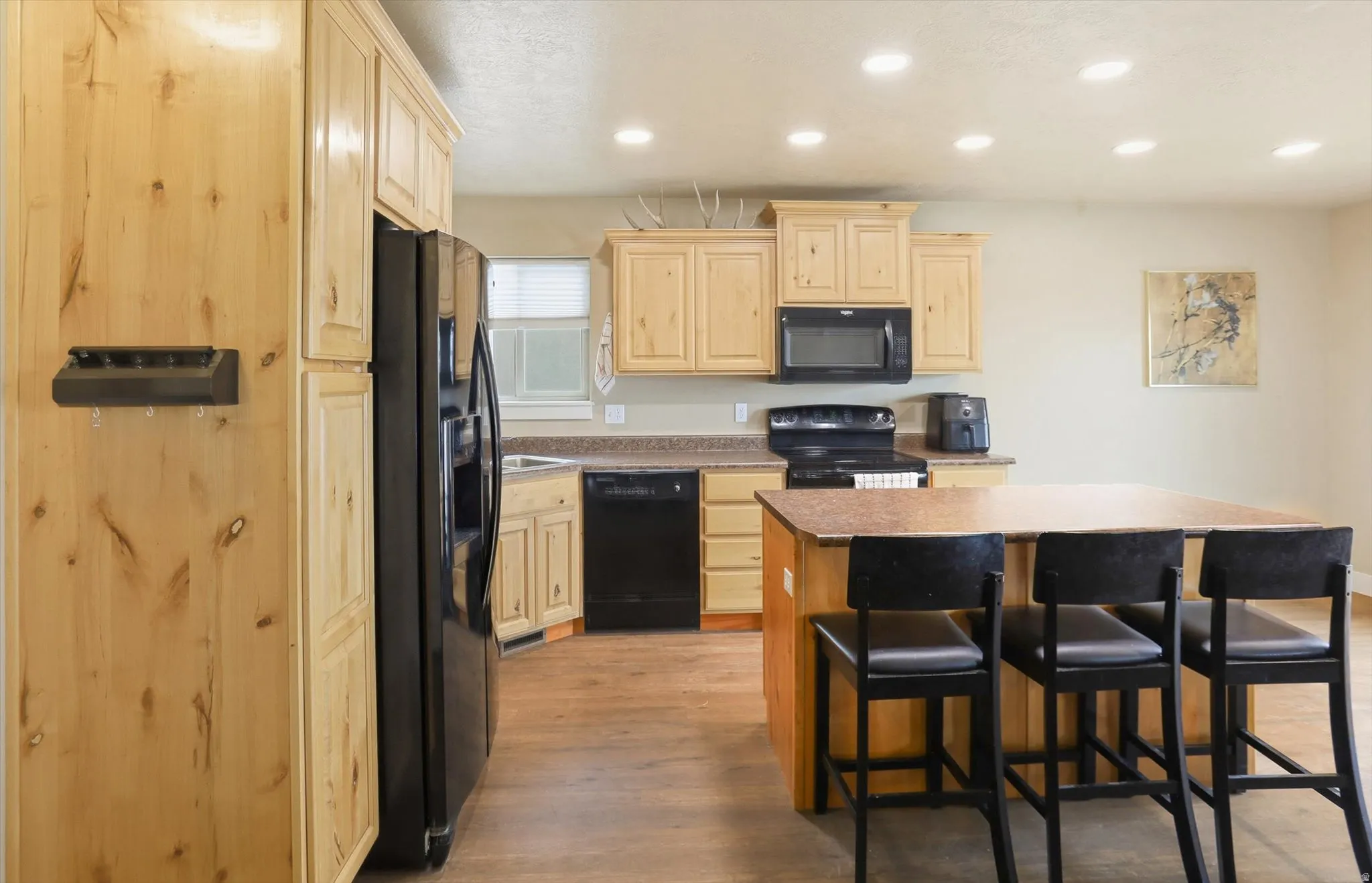 Kitchen featuring light wood finish cabinets, a kitchen island, black appliances, light wood-style floors, and a breakfast bar area