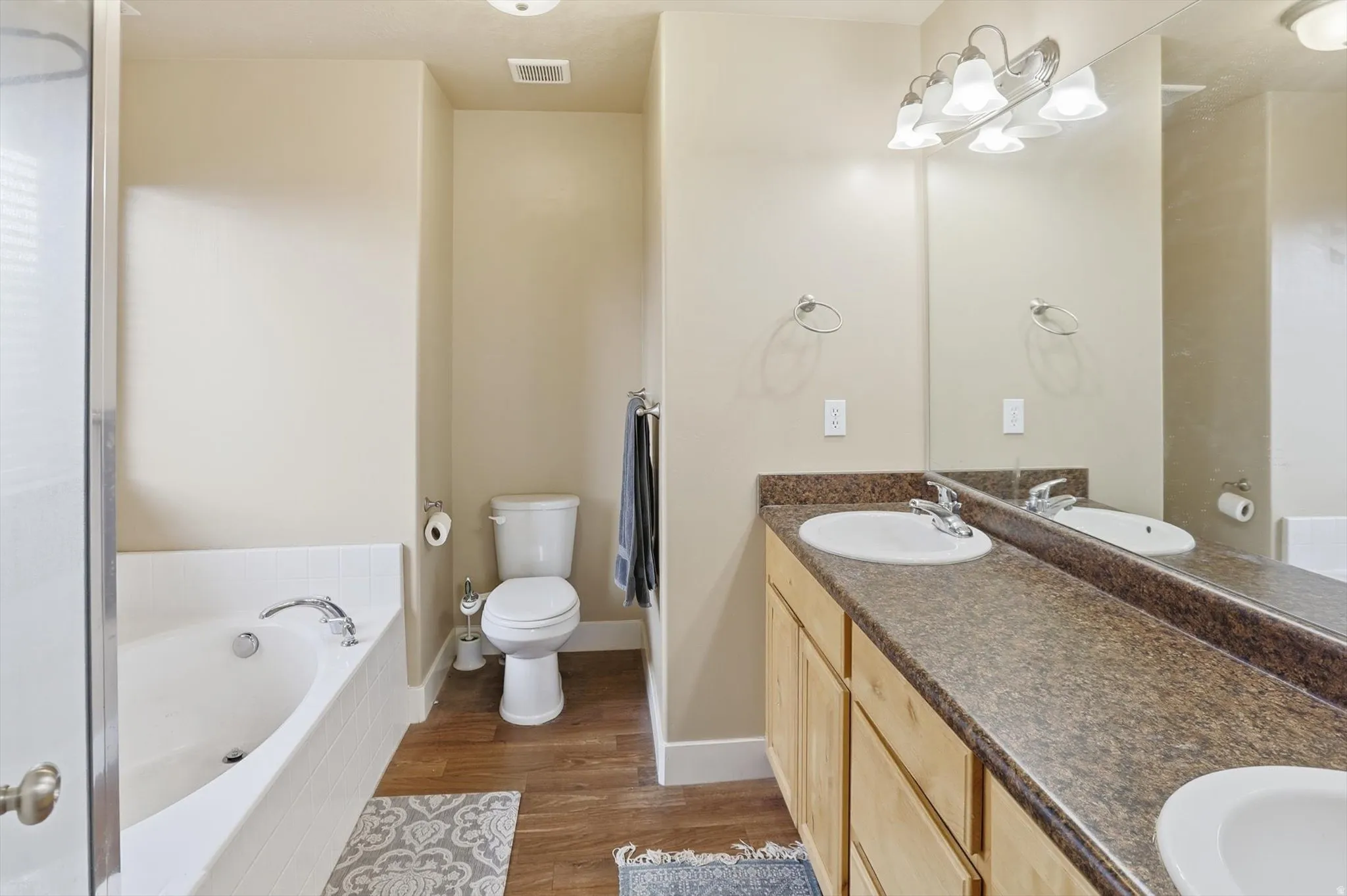 Full bath with double vanity, dark wood finished floors, and a bath