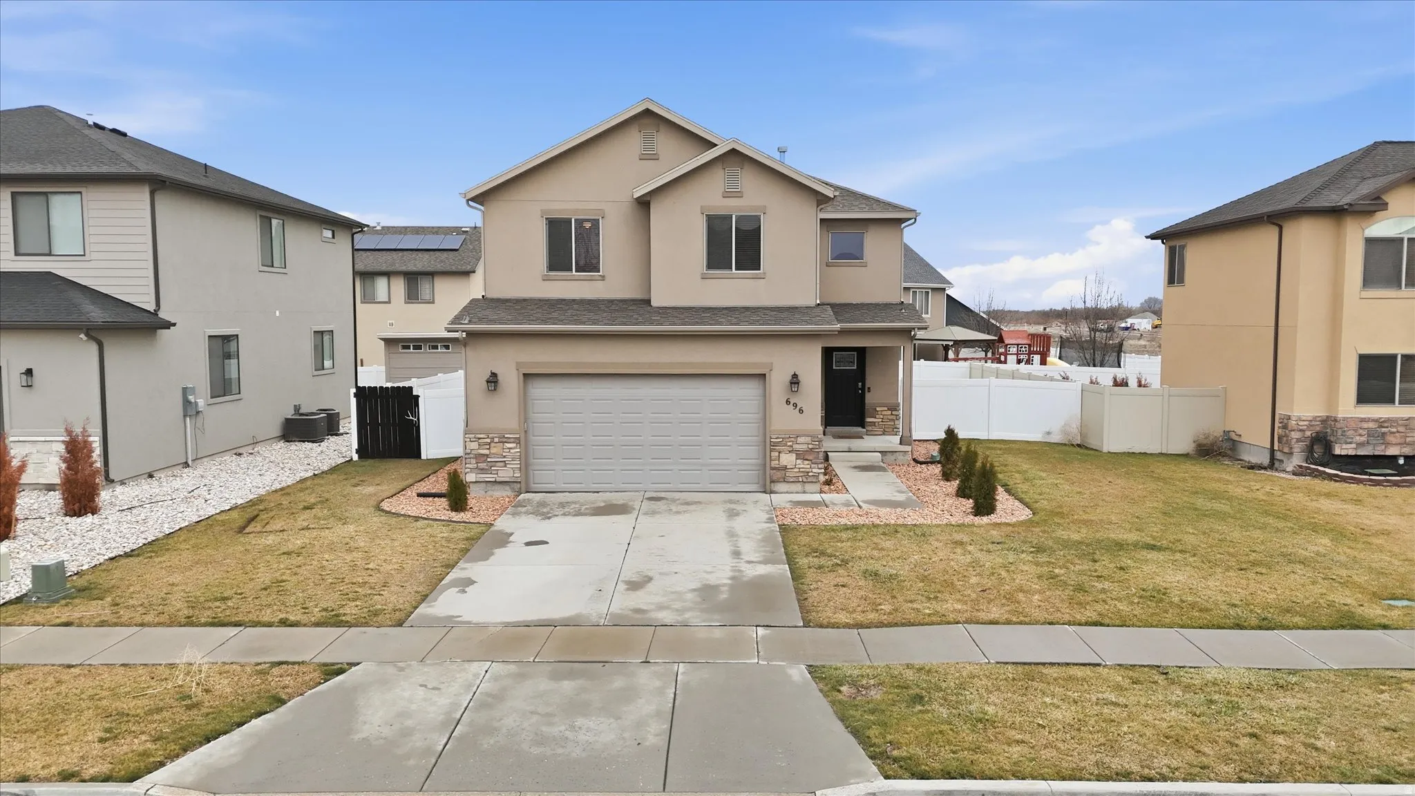 Traditional home with an attached garage, driveway, stucco siding, stone siding, and a gate