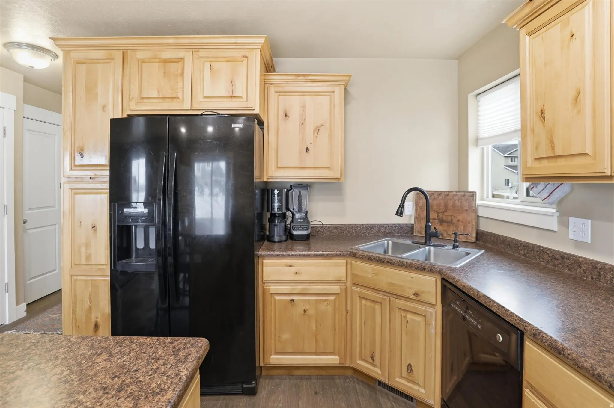 Kitchen with dark countertops, black appliances, light wood finish cabinetry, and dark wood-style flooring