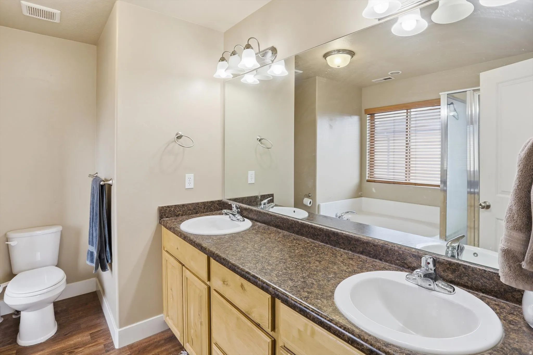 Full bath with a bath, a stall shower, double vanity, and dark wood-type flooring