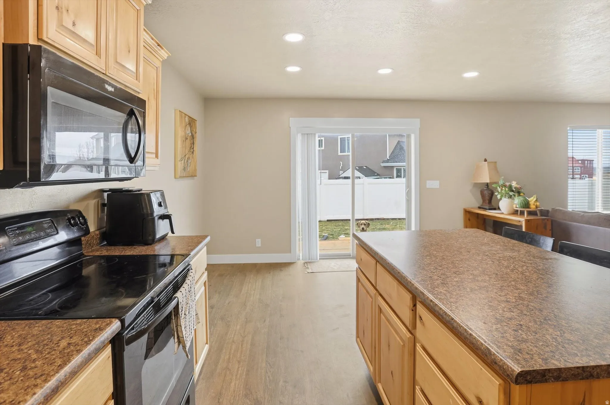 Kitchen featuring light wood finish cabinetry, black appliances, dark countertops, a center island, and recessed lighting