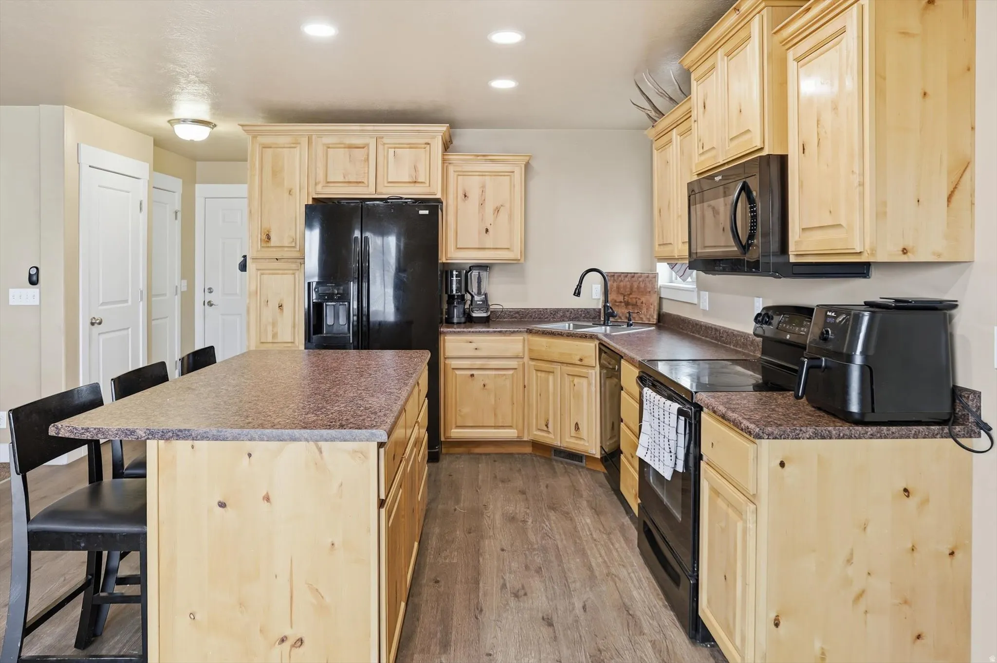 Kitchen featuring light wood finish cabinetry, a kitchen breakfast bar, black appliances, dark countertops, and recessed lighting