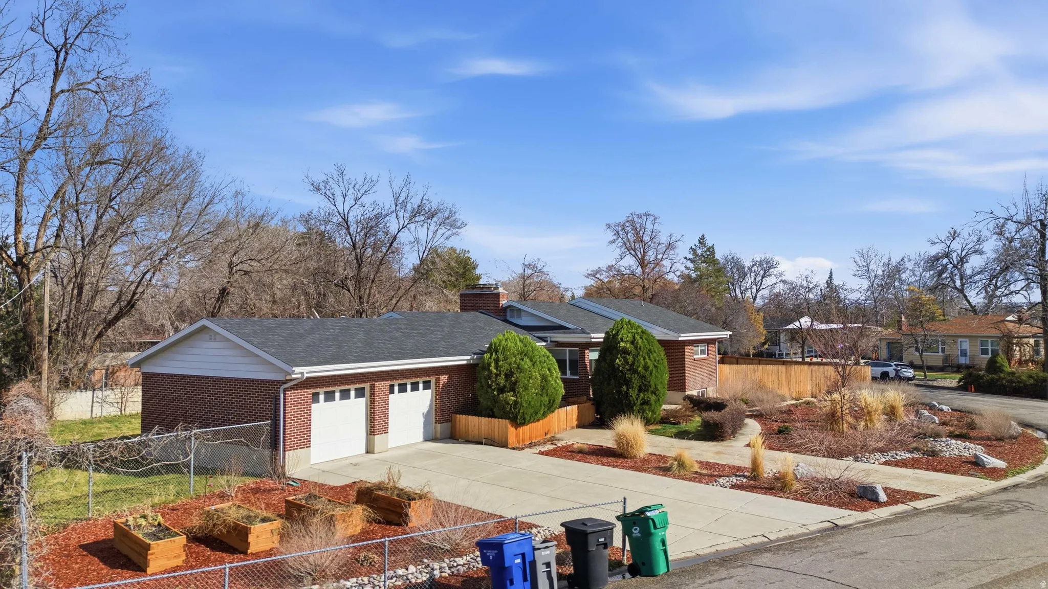 Ranch-style home with a fenced front yard, brick siding, driveway, a garden, and an attached garage