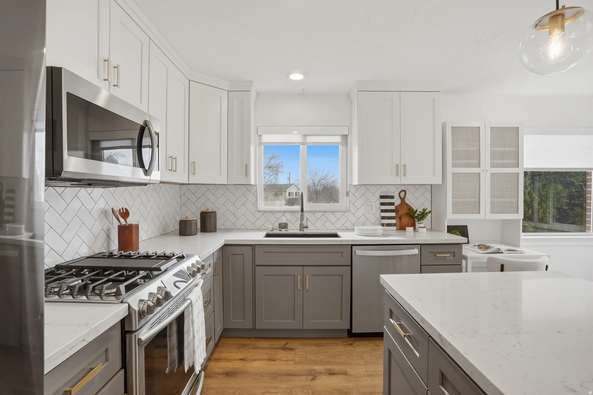 Kitchen featuring stainless steel appliances, two tone cabinets, light stone countertops, light wood finished floors, and pendant lighting
