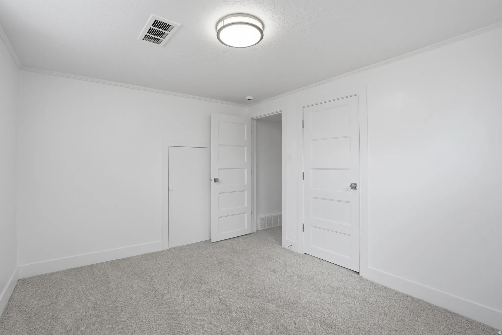 Downstairs bedroom with light colored carpet and crown molding