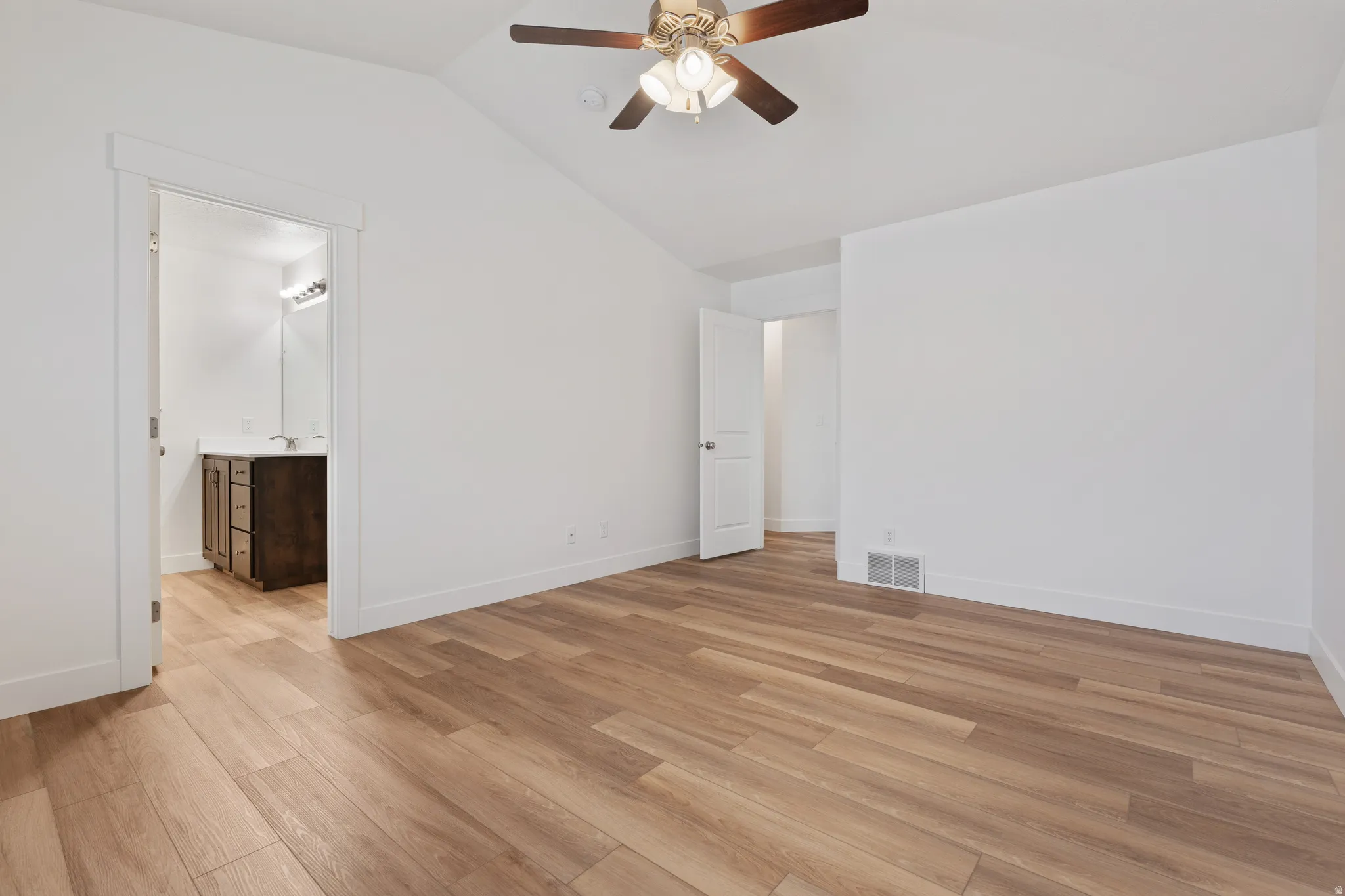 Unfurnished bedroom featuring ceiling fan, vaulted ceiling, light wood finished floors, and connected bathroom