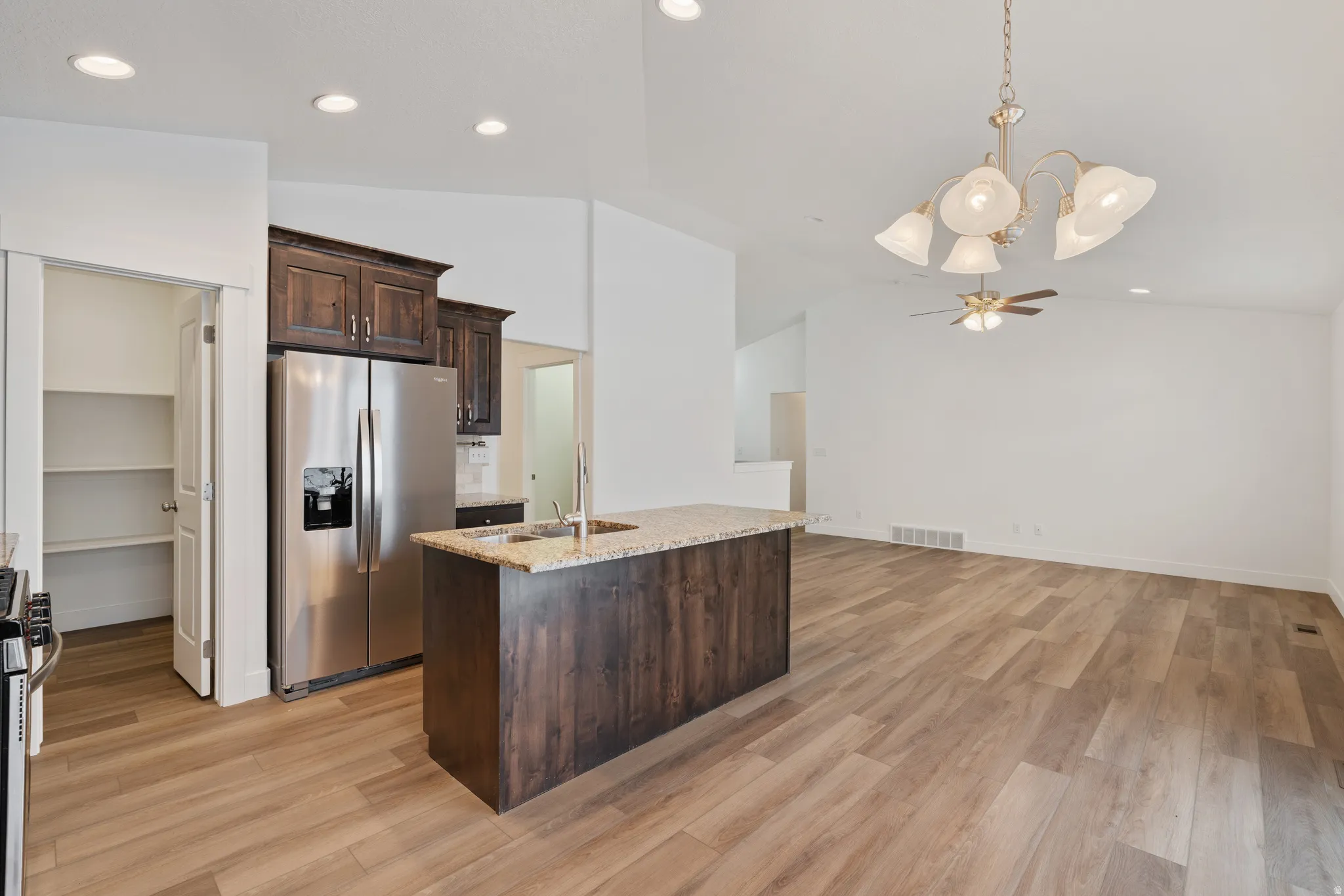 Kitchen featuring stainless steel appliances, dark wood finish cabinets, light stone counters, a center island with sink, and light wood-style flooring