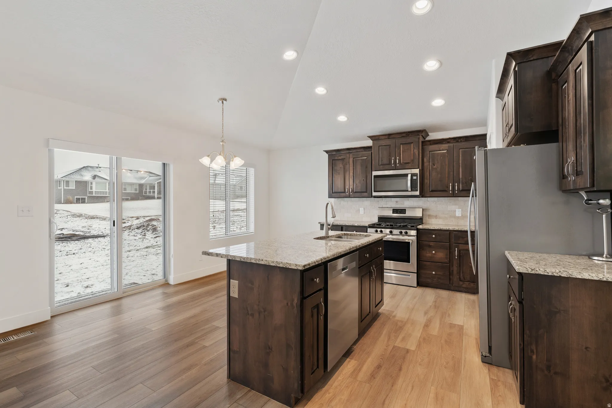 Kitchen with lofted ceiling, dark wood finish cabinets, stainless steel appliances, light stone countertops, and backsplash