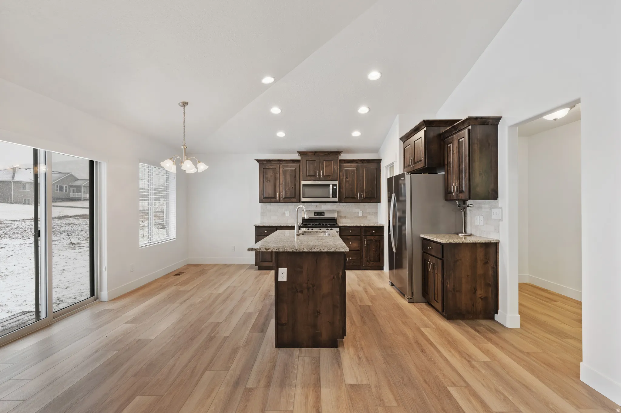 Kitchen with vaulted ceiling, dark wood finish cabinets, decorative backsplash, stainless steel appliances, and suspended lighting