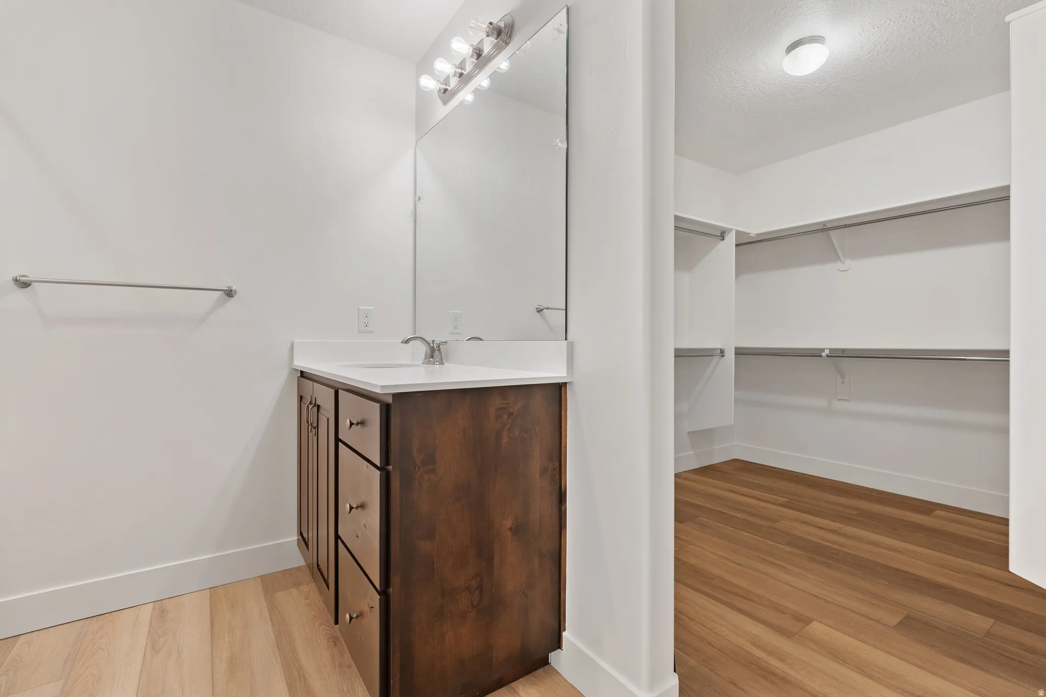 Bathroom featuring vanity, light wood-style flooring, a walk in closet, and a textured ceiling