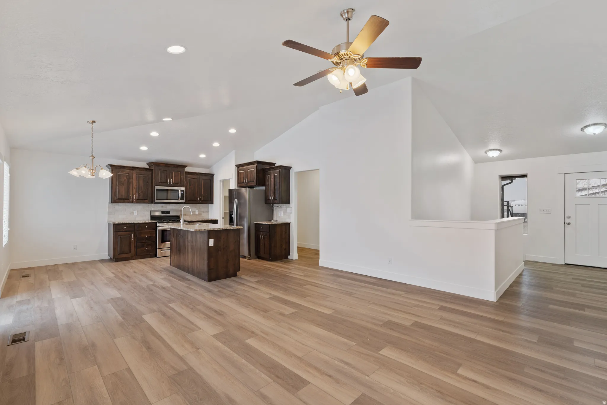 Kitchen featuring dark wood finish cabinetry, open floor plan, a center island with sink, stainless steel appliances, and decorative backsplash