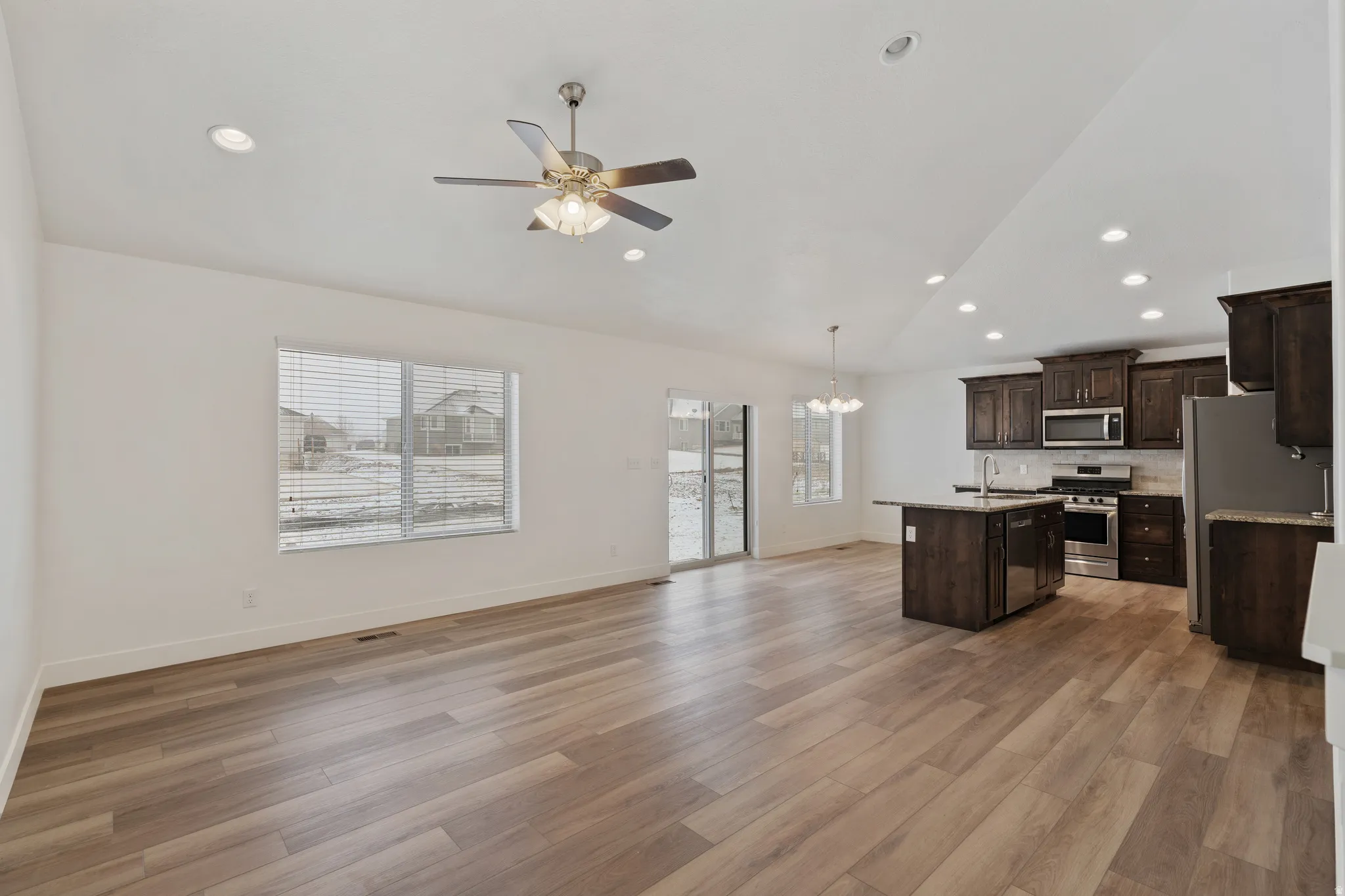 Kitchen featuring dark wood finish cabinets, ceiling fan, open floor plan, stainless steel appliances, and plenty of natural light