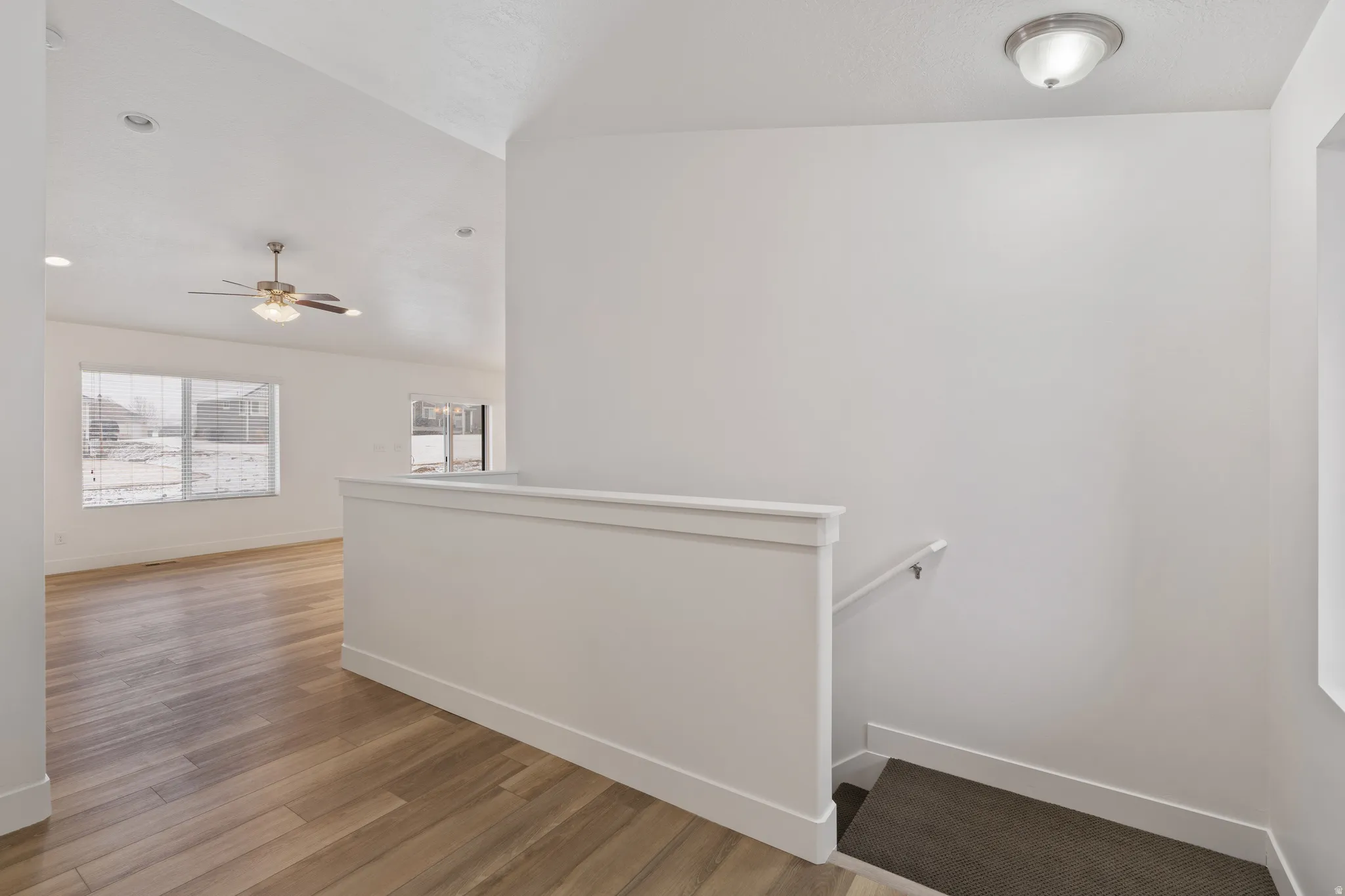 Corridor with light wood finished floors, vaulted ceiling, and an upstairs landing